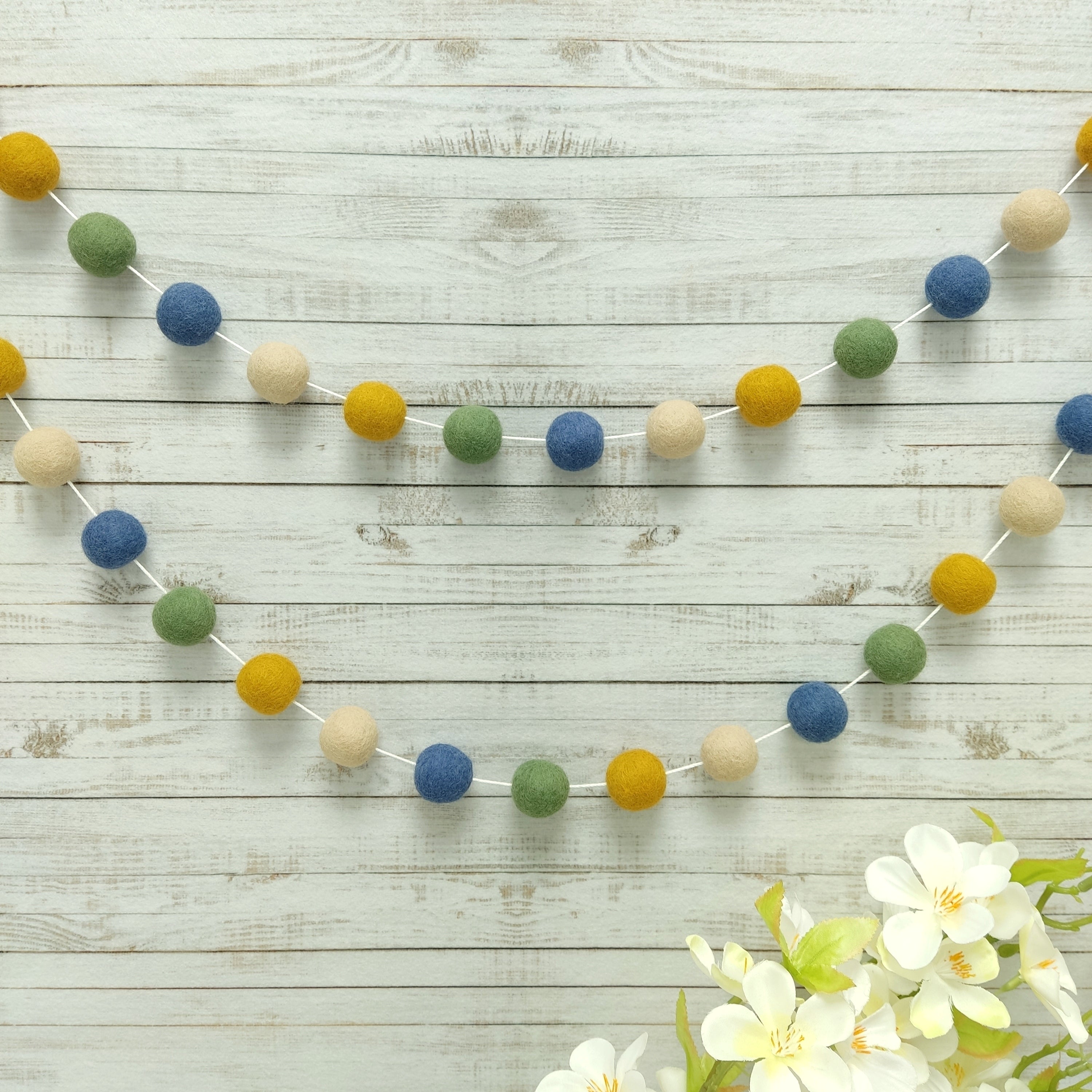 Guirlande pompons en feutre vert jaune bleu beige fixée sur un mur de chambre 