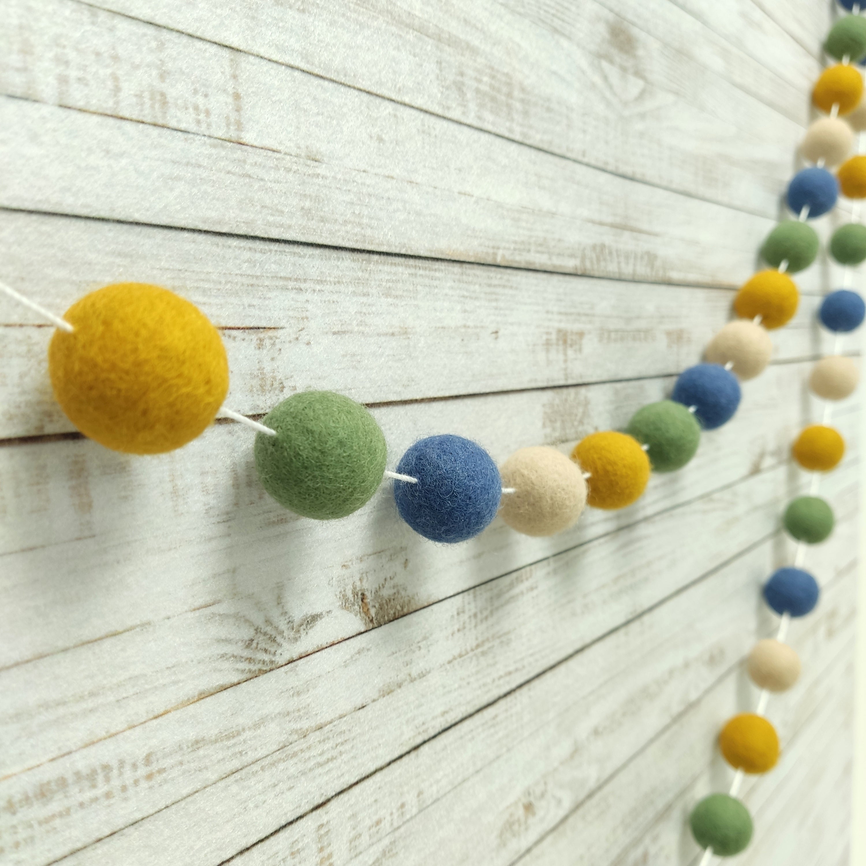 Vue de profil de la guirlande matcha ocre en pompons feutrés