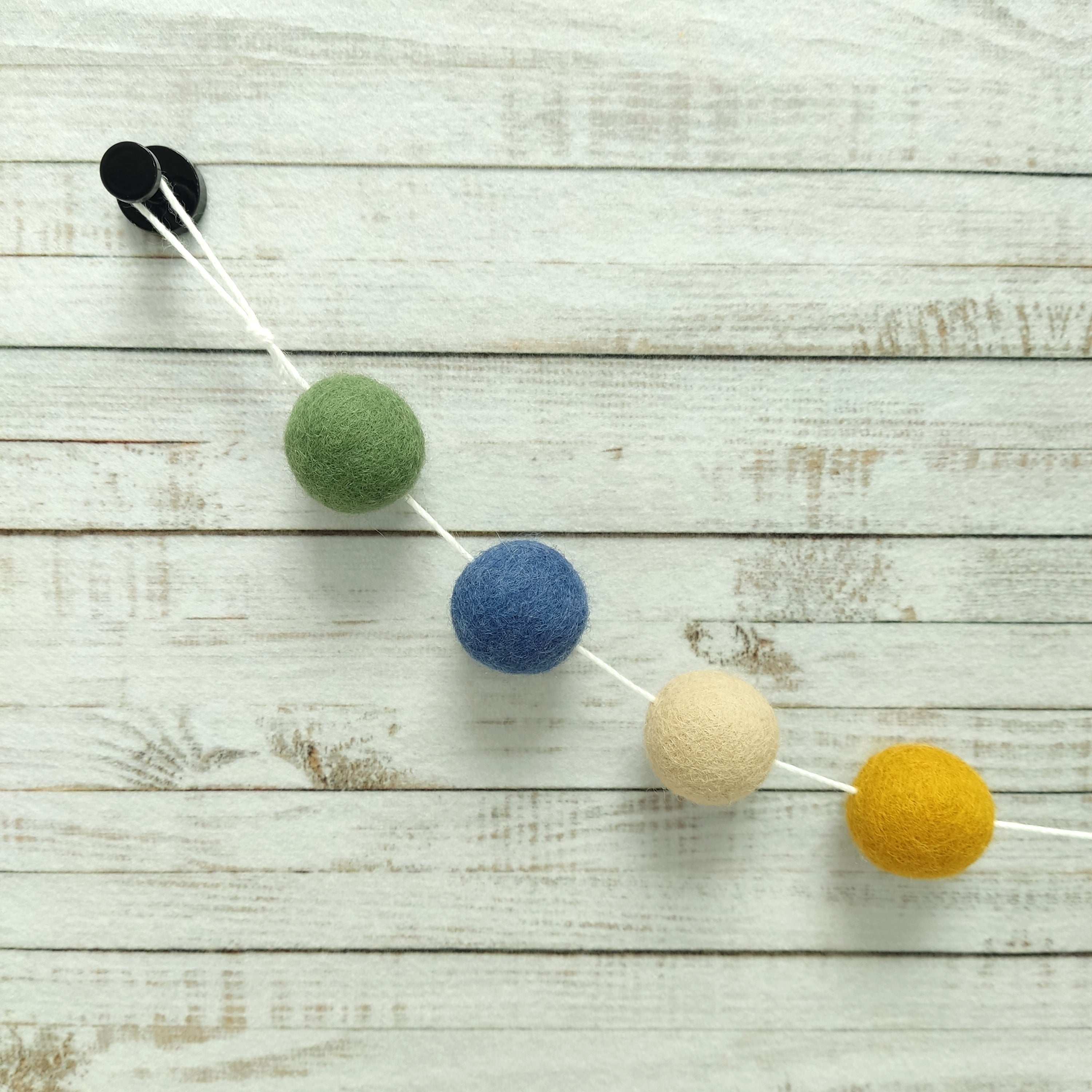 Détails des 4 couleurs de pompons en feutre ocre doré, beige poudré, bleu denim et vert matcha