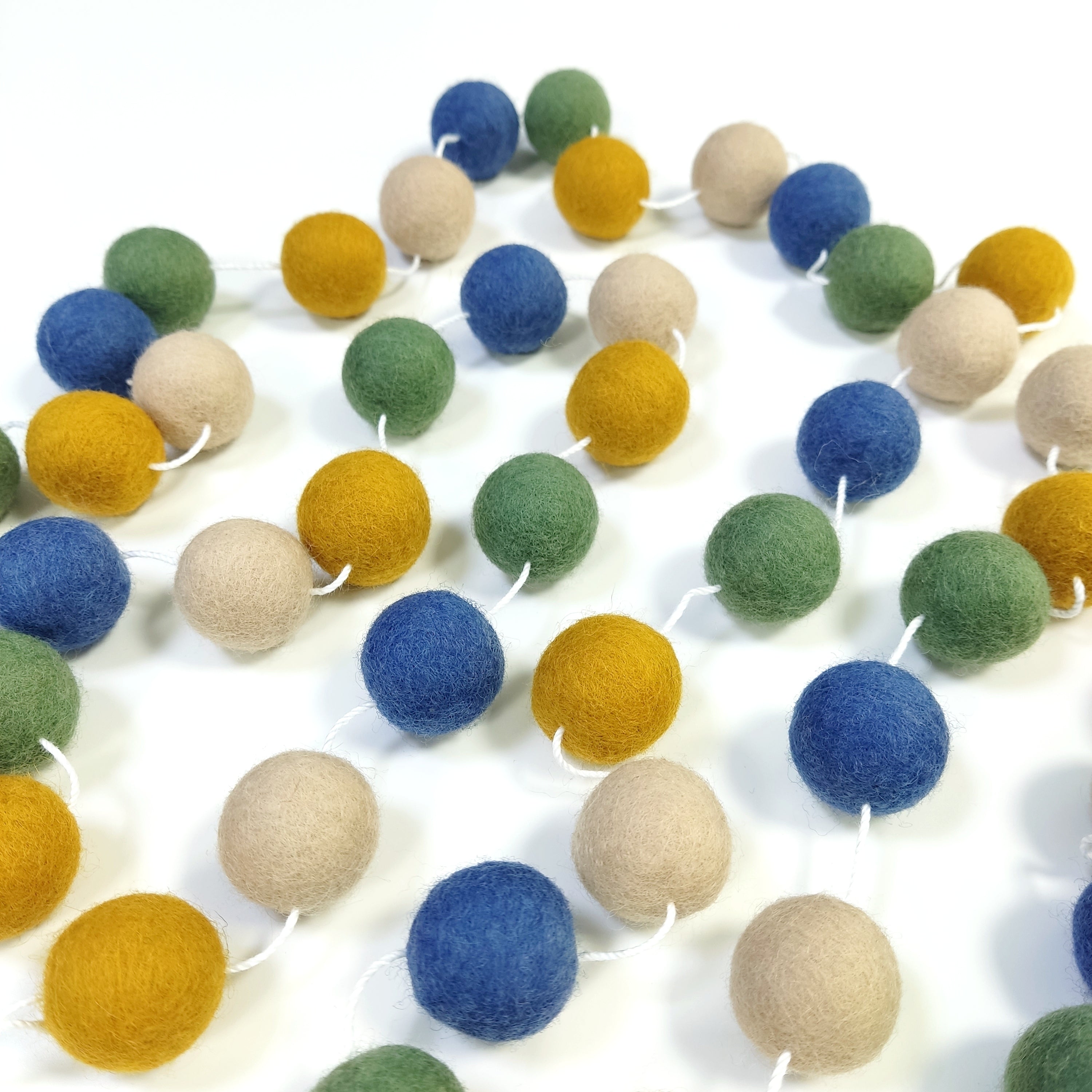 Guirlande en boules de laine feutrée vert bleu jaune beige étalée sur une table