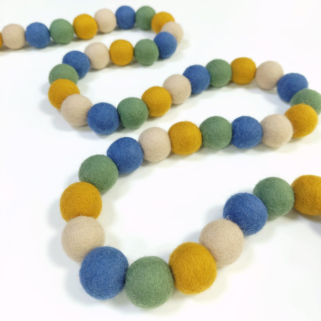 Guirlande de boules de feutre vert jaune bleu beige disposée en serpentin sur une table