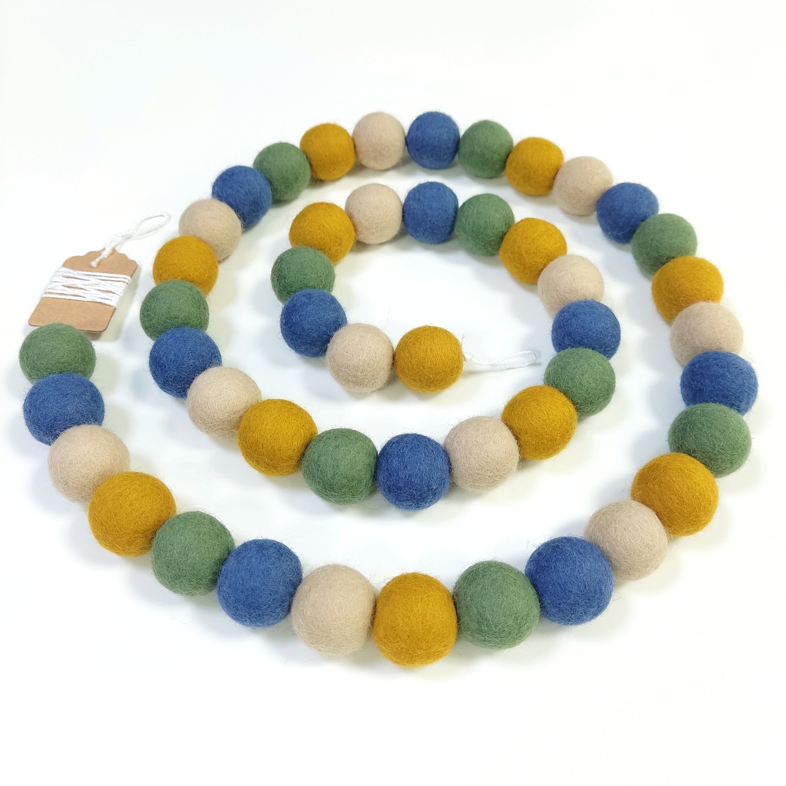 Guirlande de pompons de feutre matcha ocre posée en forme de spirale vue de dessus