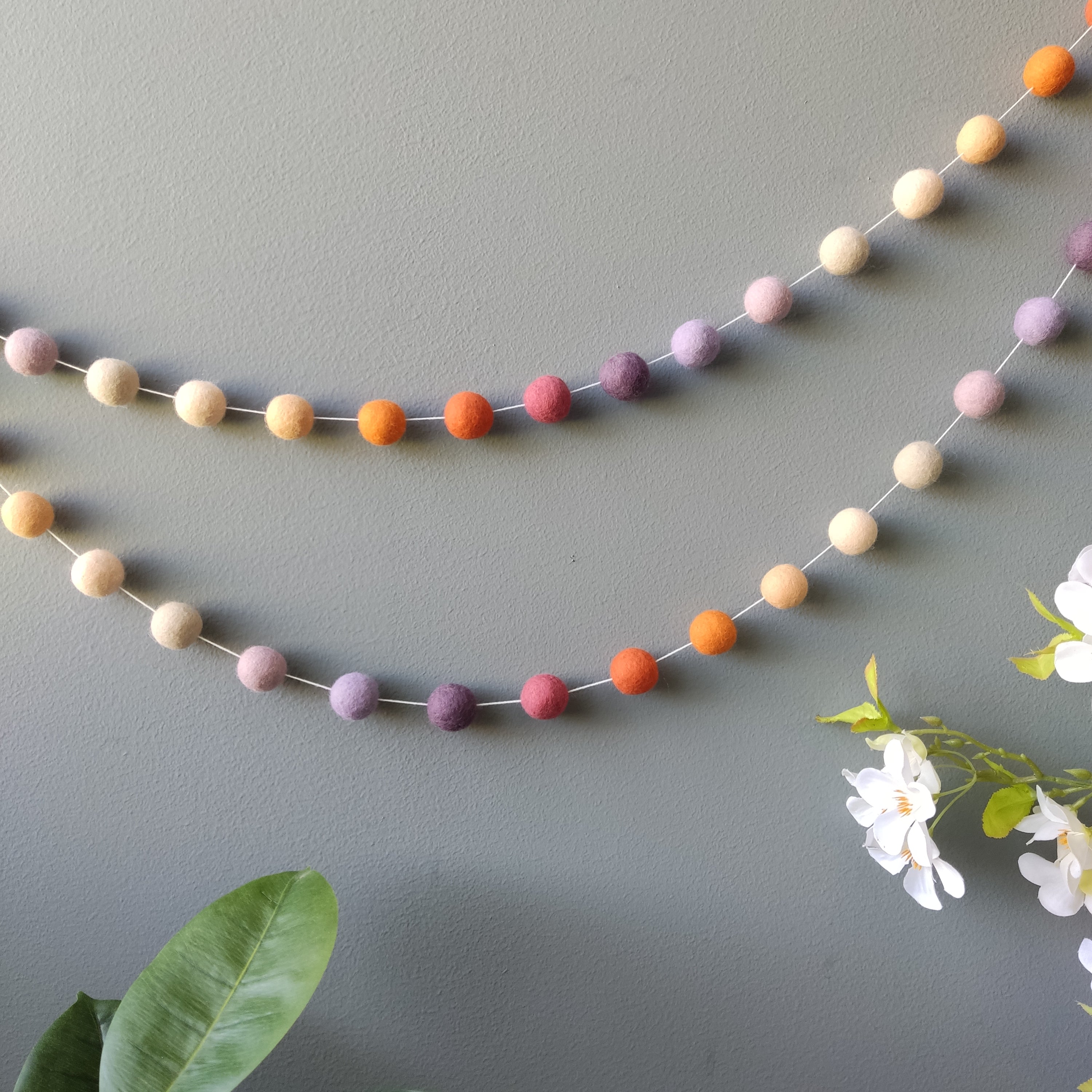 Guirlande pompons teintes mauve beige et orange en décoration murale