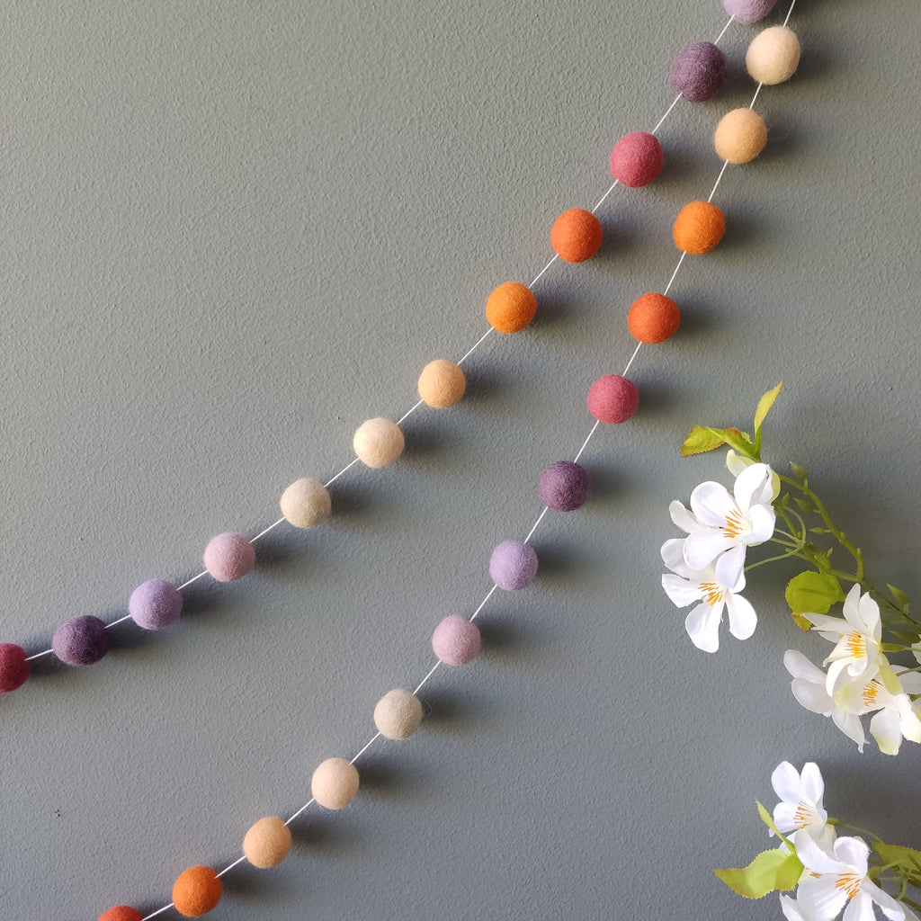 Guirlande en boules de feutre laine mérinos mauve et orange accrochée au mur