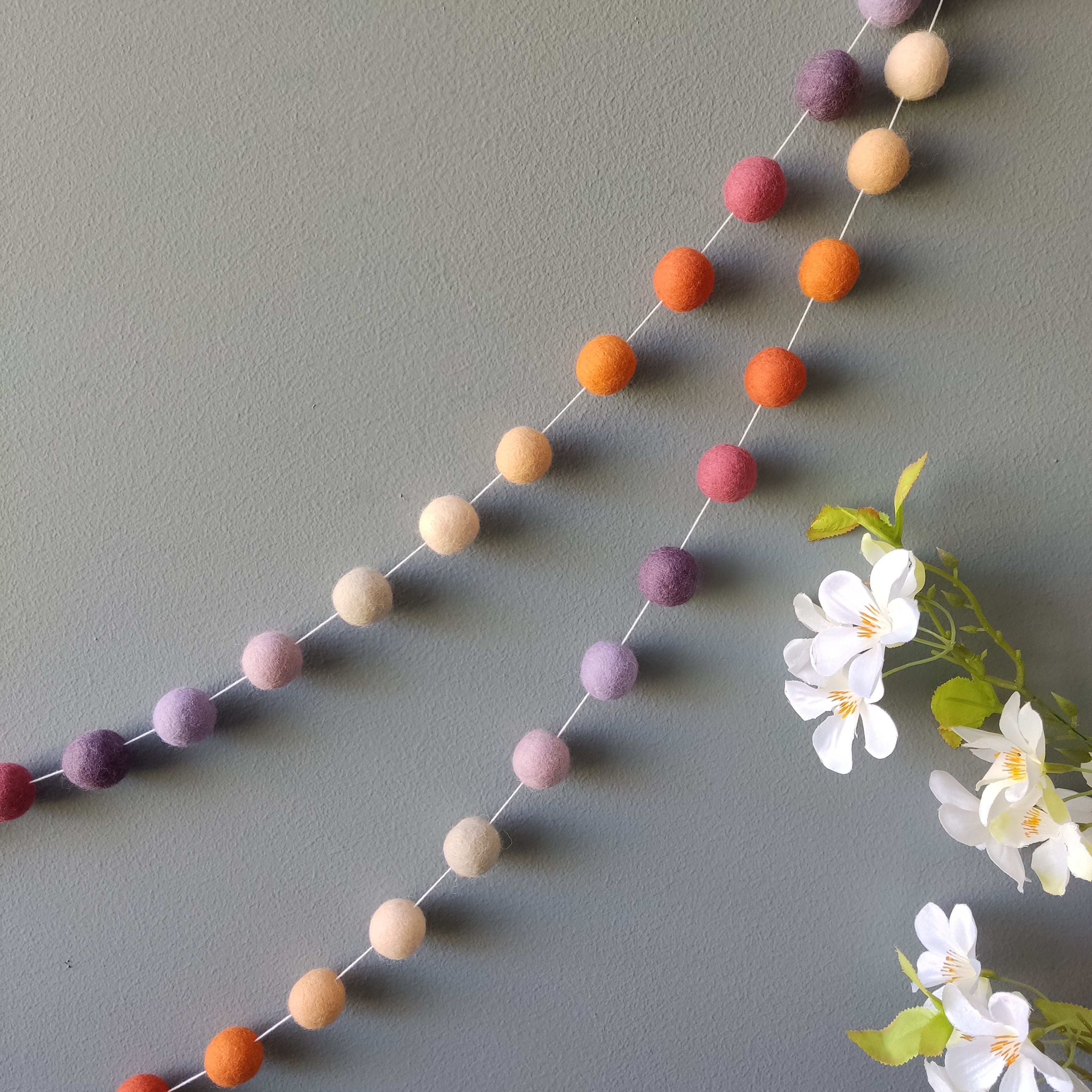 Guirlande en boules de feutre laine mérinos mauve et orange accrochée au mur