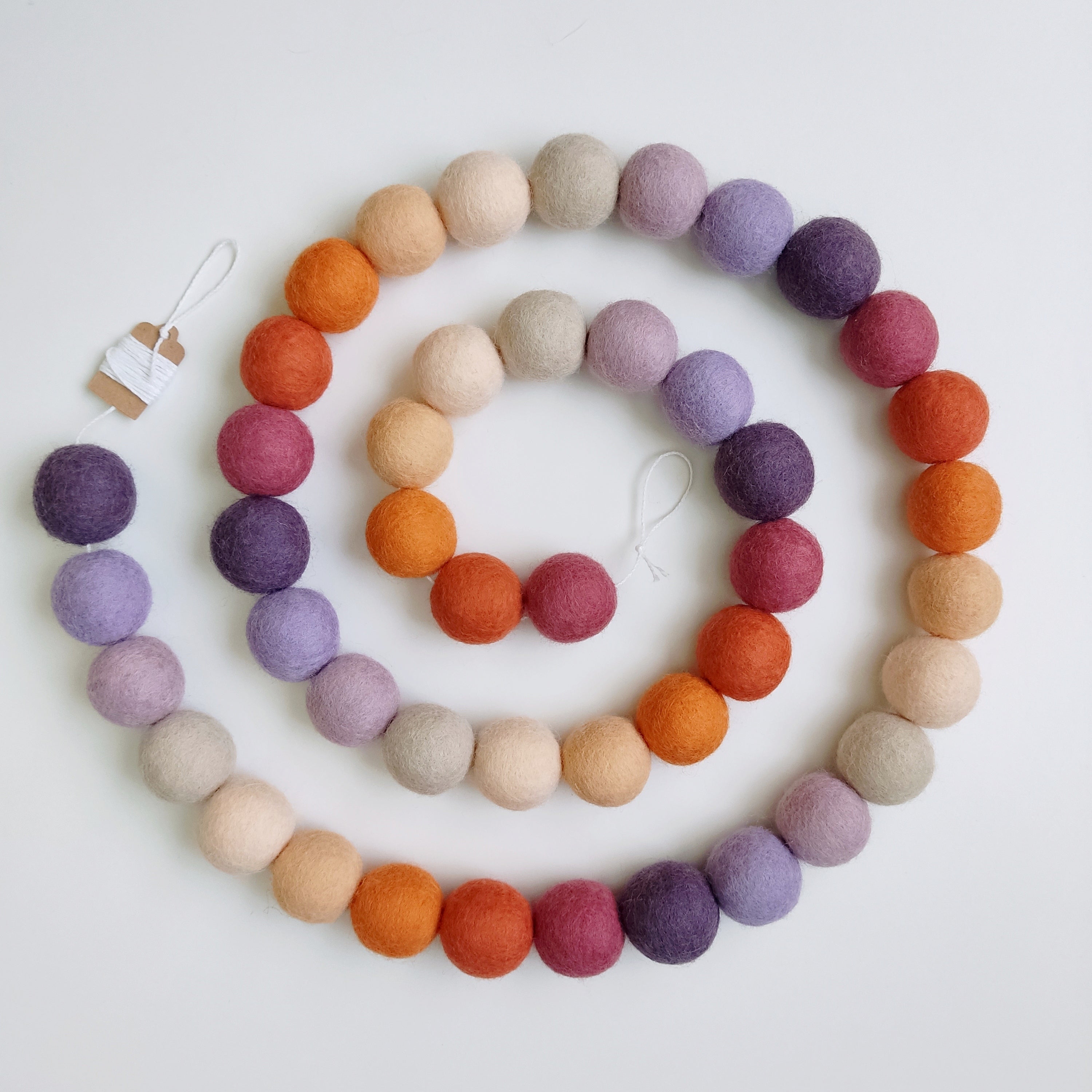 Guirlande en boules de feutre beige, mauve, orange, violet et rose posée en spirale sur une table
