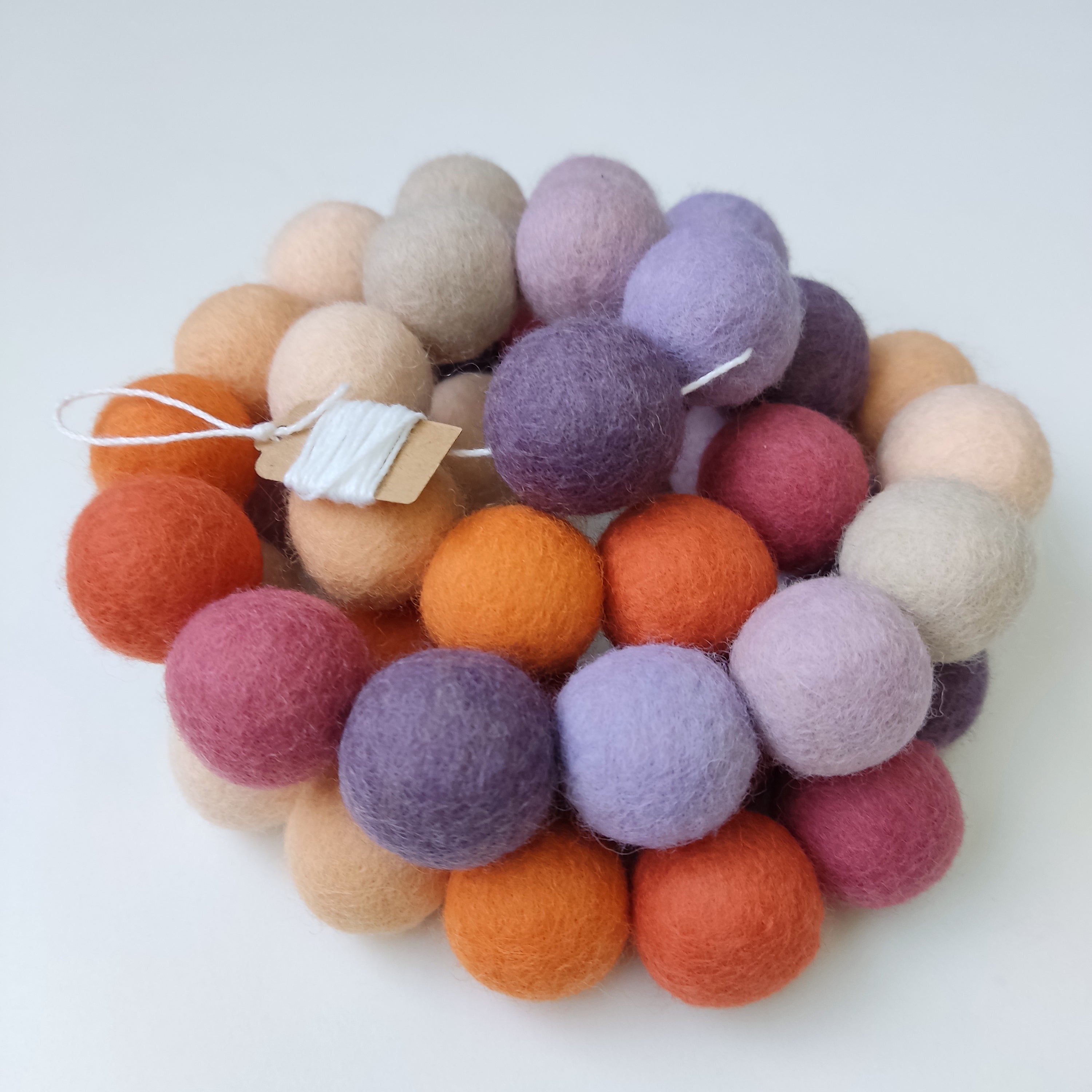 Guirlande de boules de feutre mauve orange avec les pompons rassemblés sur le fil de coton