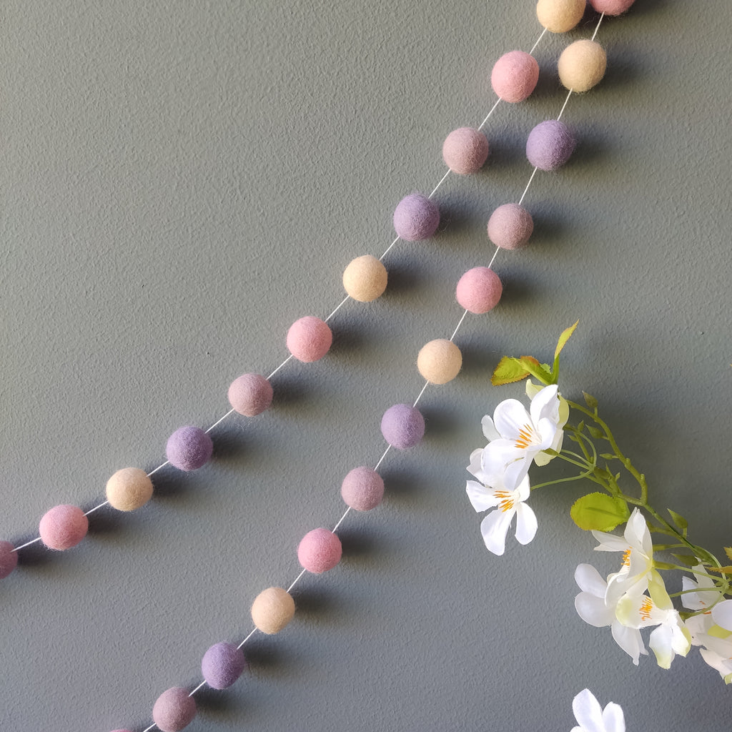 Guirlandes de pompons feutrés mauve et rose sur un mur de chambre