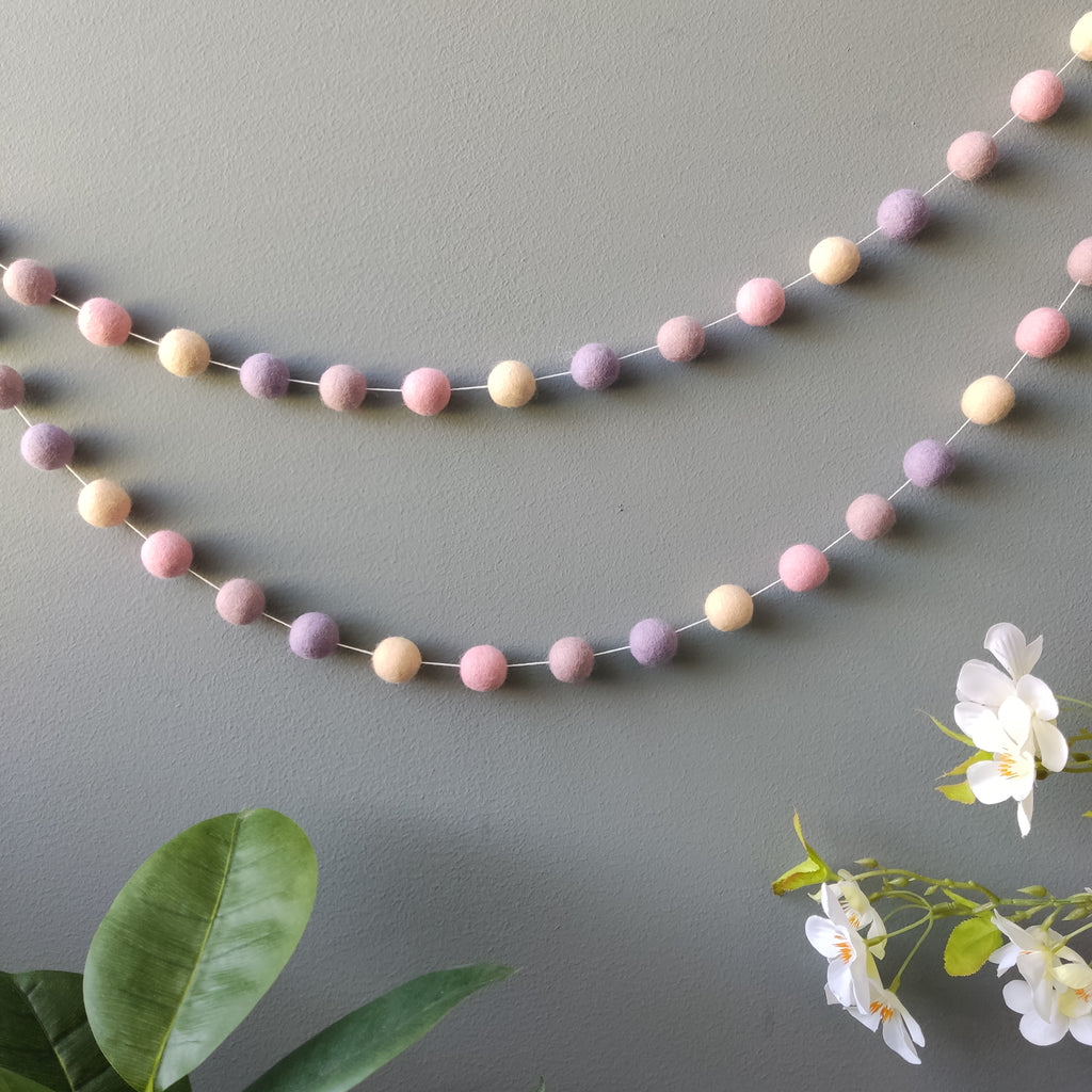 Guirlande en boules de feutres mauve et rose vue de loin accrochée au mur