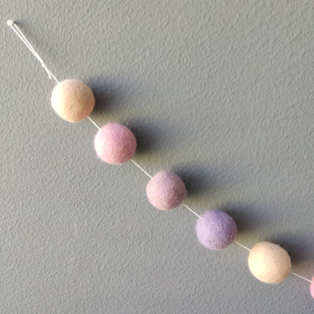 Zoom sur les pompons feutrés beige rosé, rose cerisier, lilas et mauve de la guirlande 