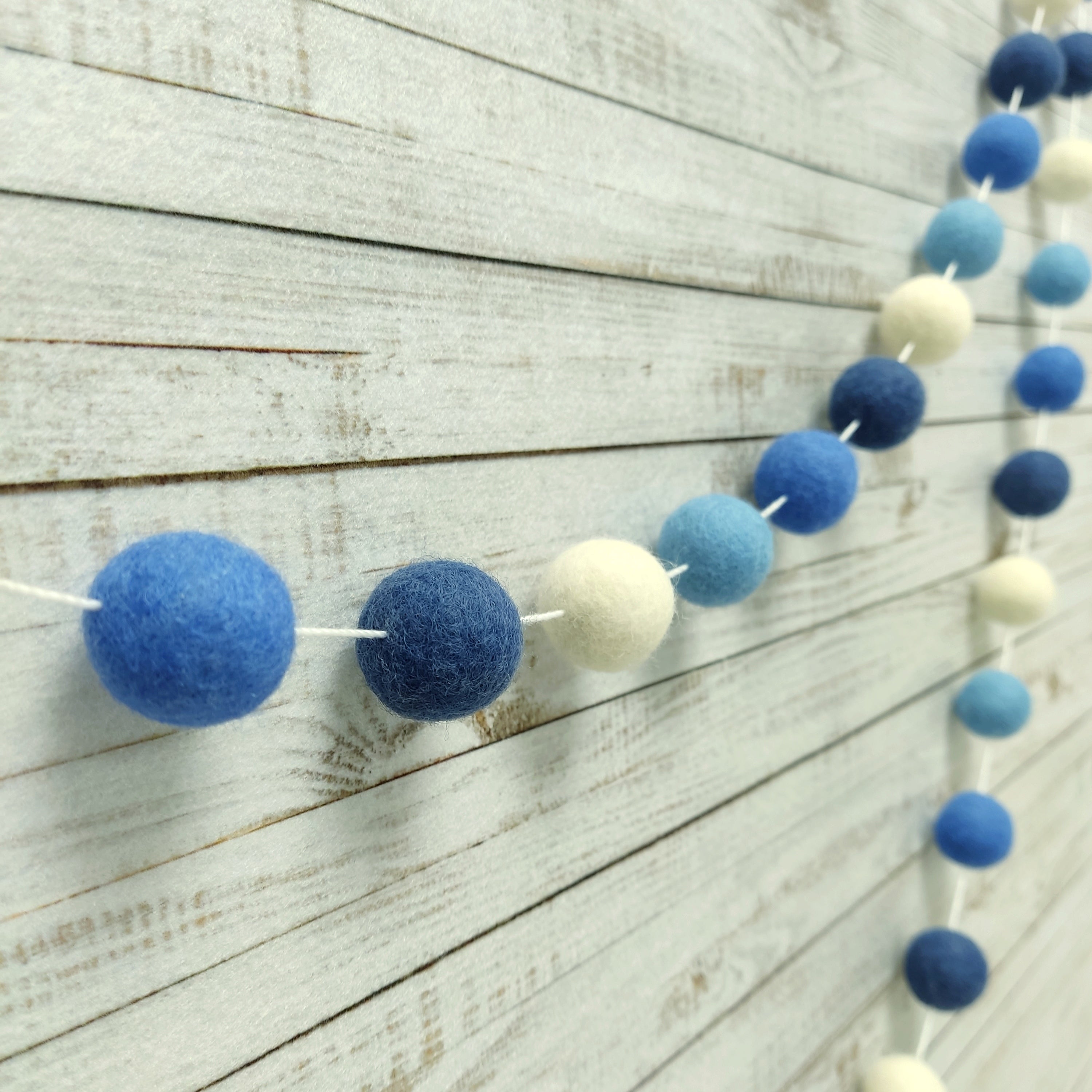 Guirlande de pompons bleu ciel, bleu lavande, bleu denim et blanc vue de profil