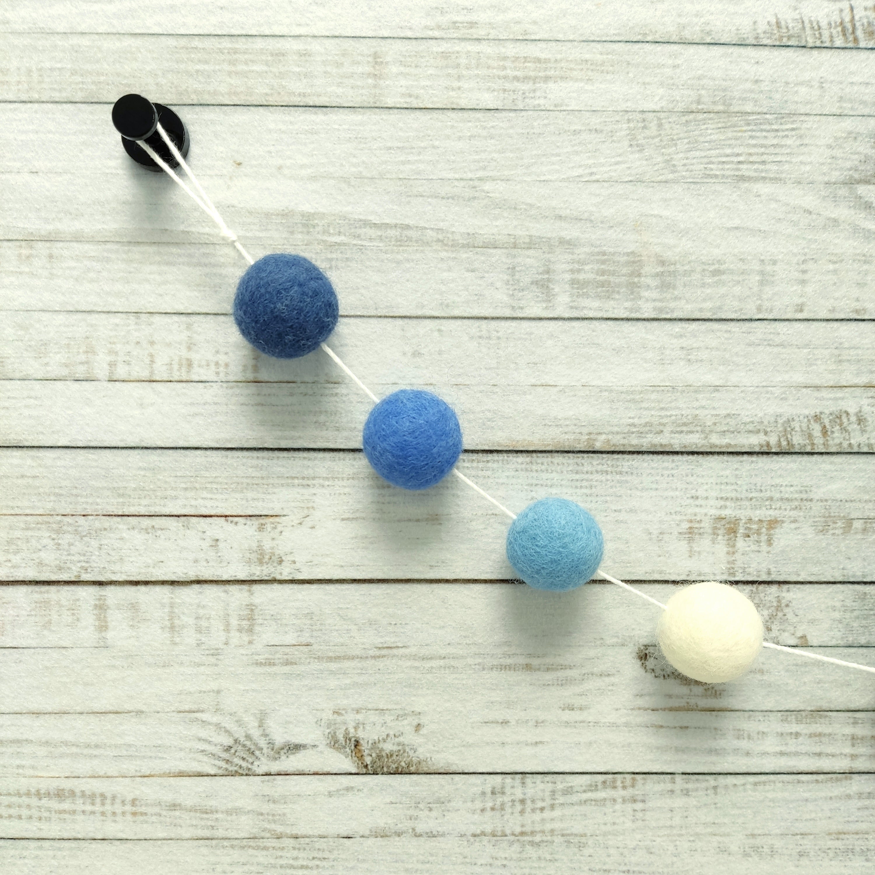 Zoom sur les pompons feutrés de laine mérinos de 2,5 cm bleu et blanc de la guirlande méditerranée