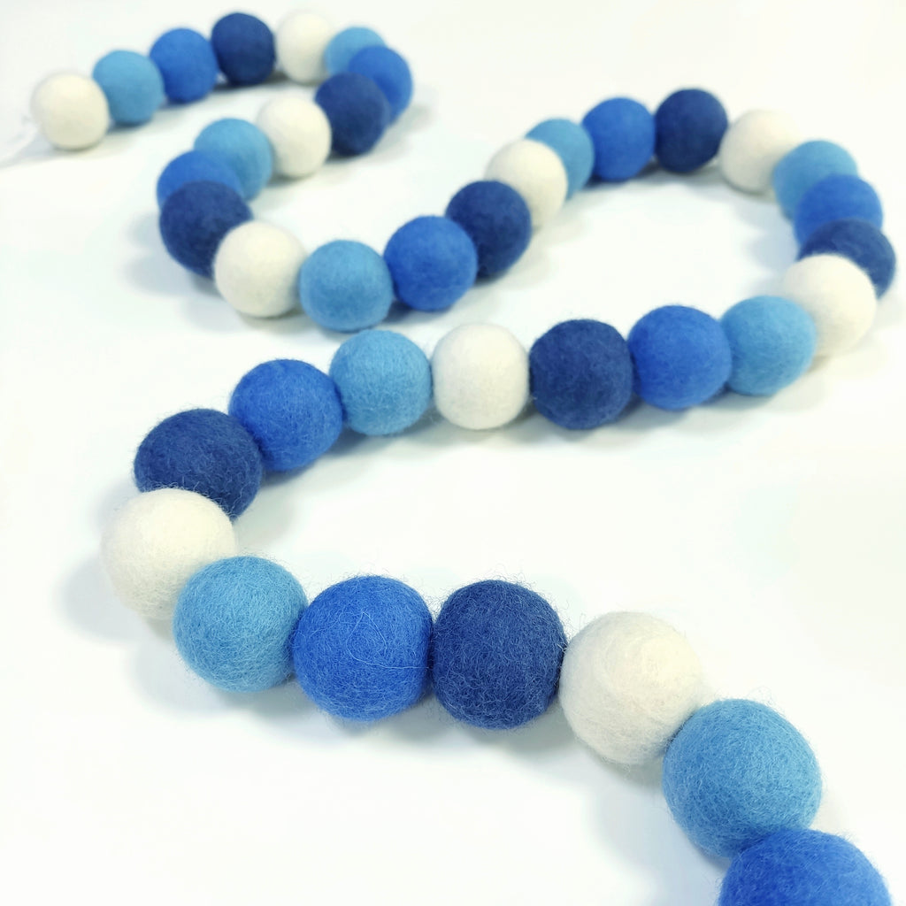 Guirlande de pompons de feutre bleu et blanc disposée en serpentin sur une table