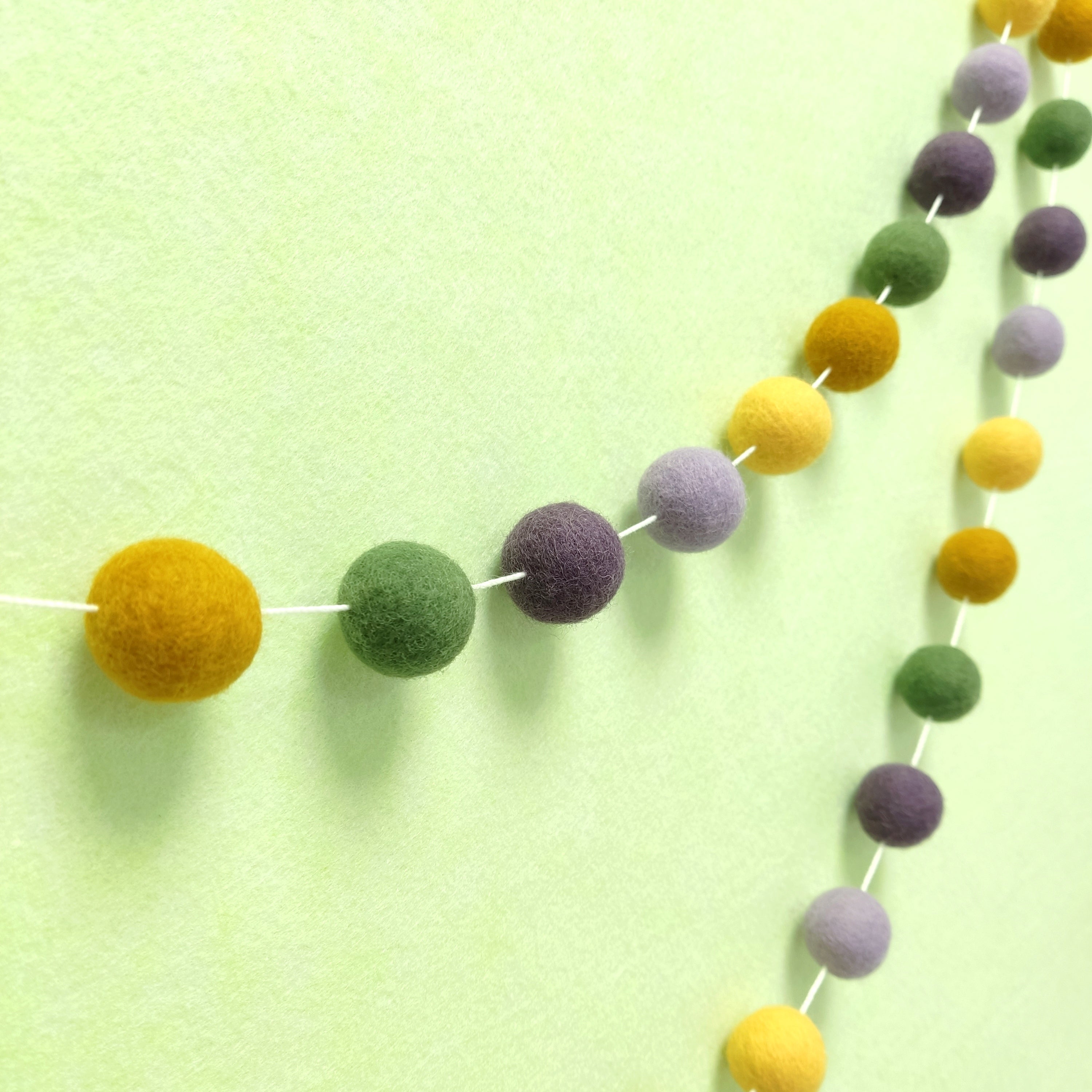 Guirlande de pompons feutrés aux teintes provençales jaune ocre, vert matcha, mauve et violet améthyste vue de profil