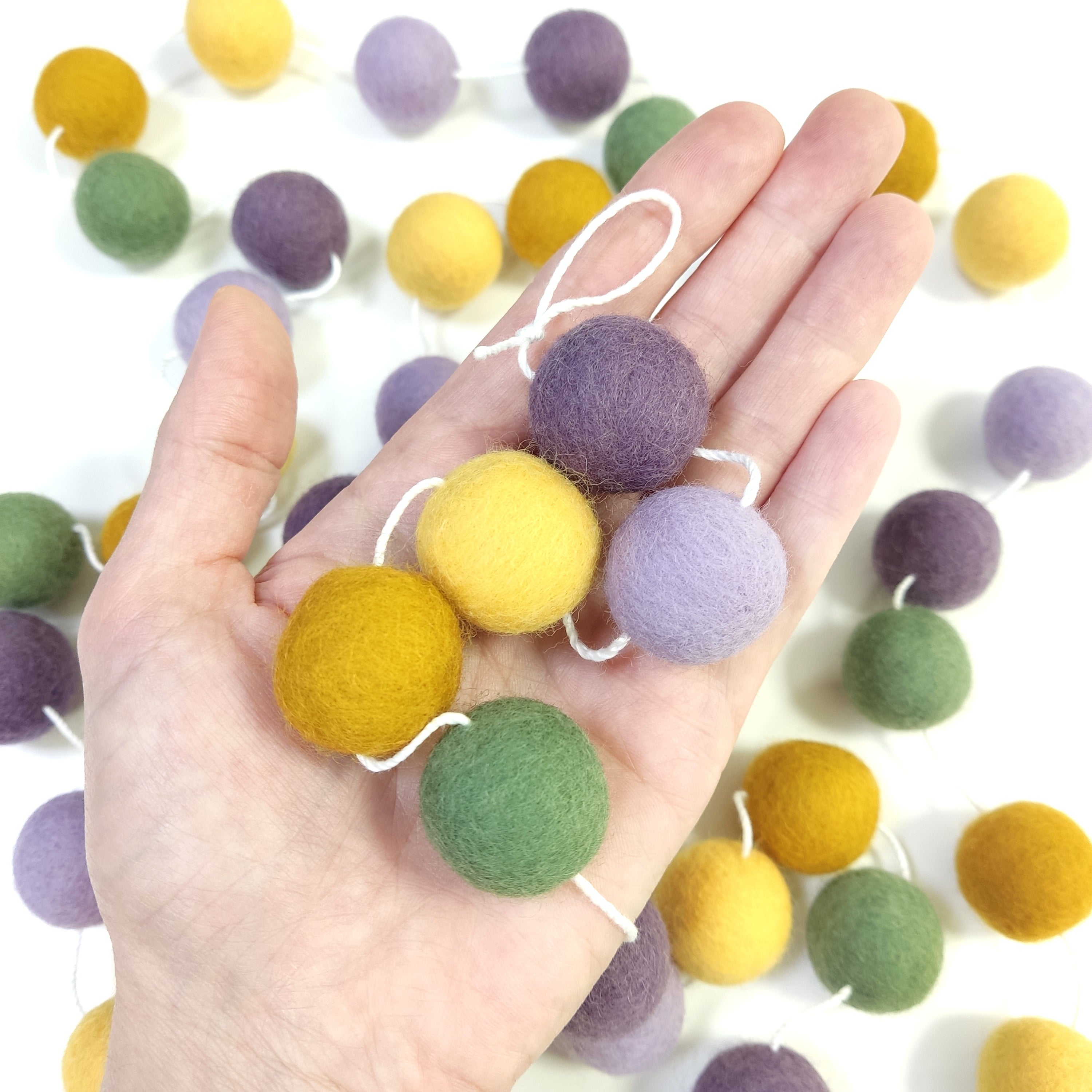 Zoom sur les pompons en laine mérinos miel lavande dans une main, teintes naturelles et provençales