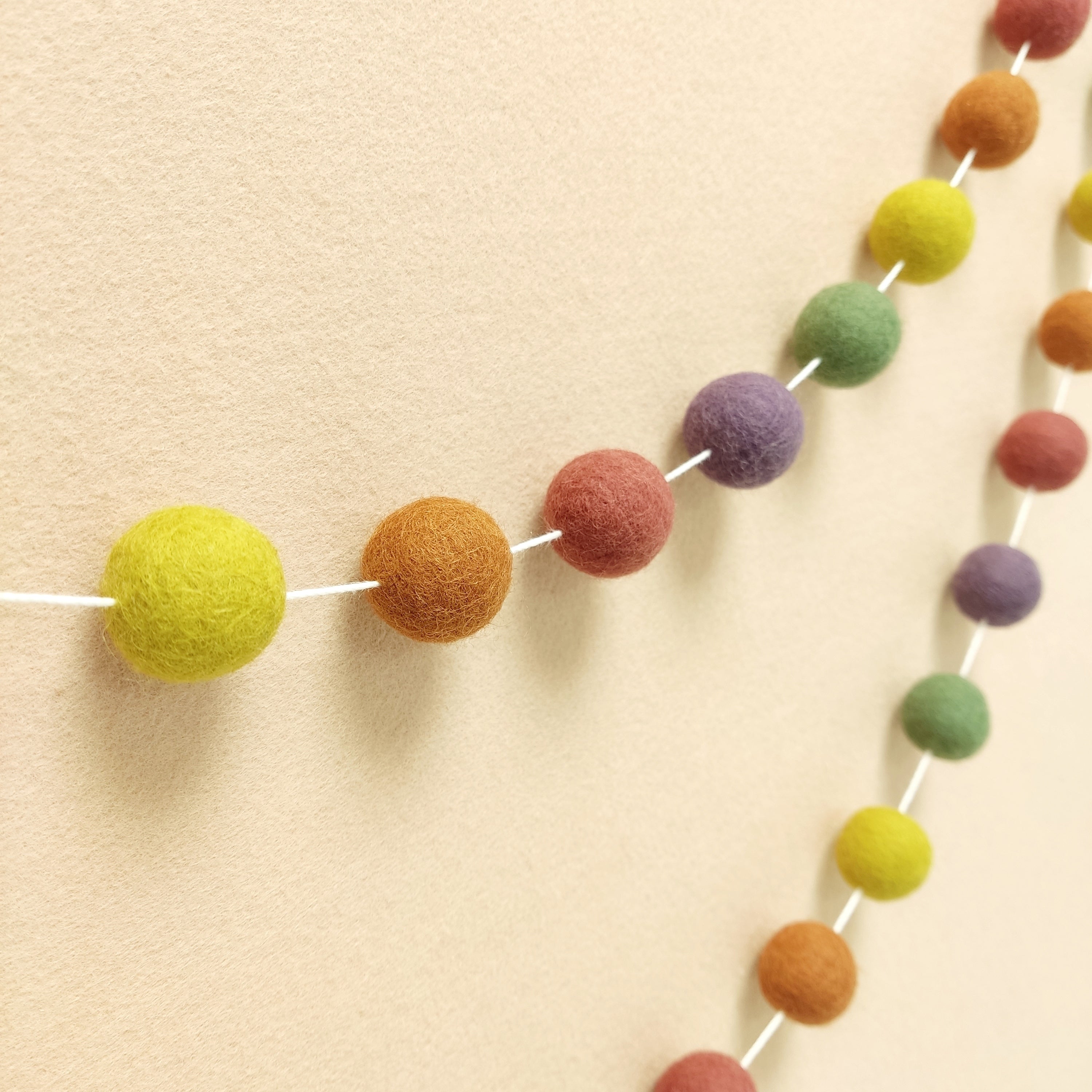 Guirlande de pompons en feutre multicolore vintage vue de profil sur un mur