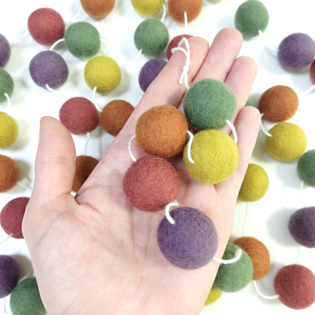 Zoom sur les pompons en feutre de laine mérinos de 2,5 cm de la guirlande multicolore vintage dans une main