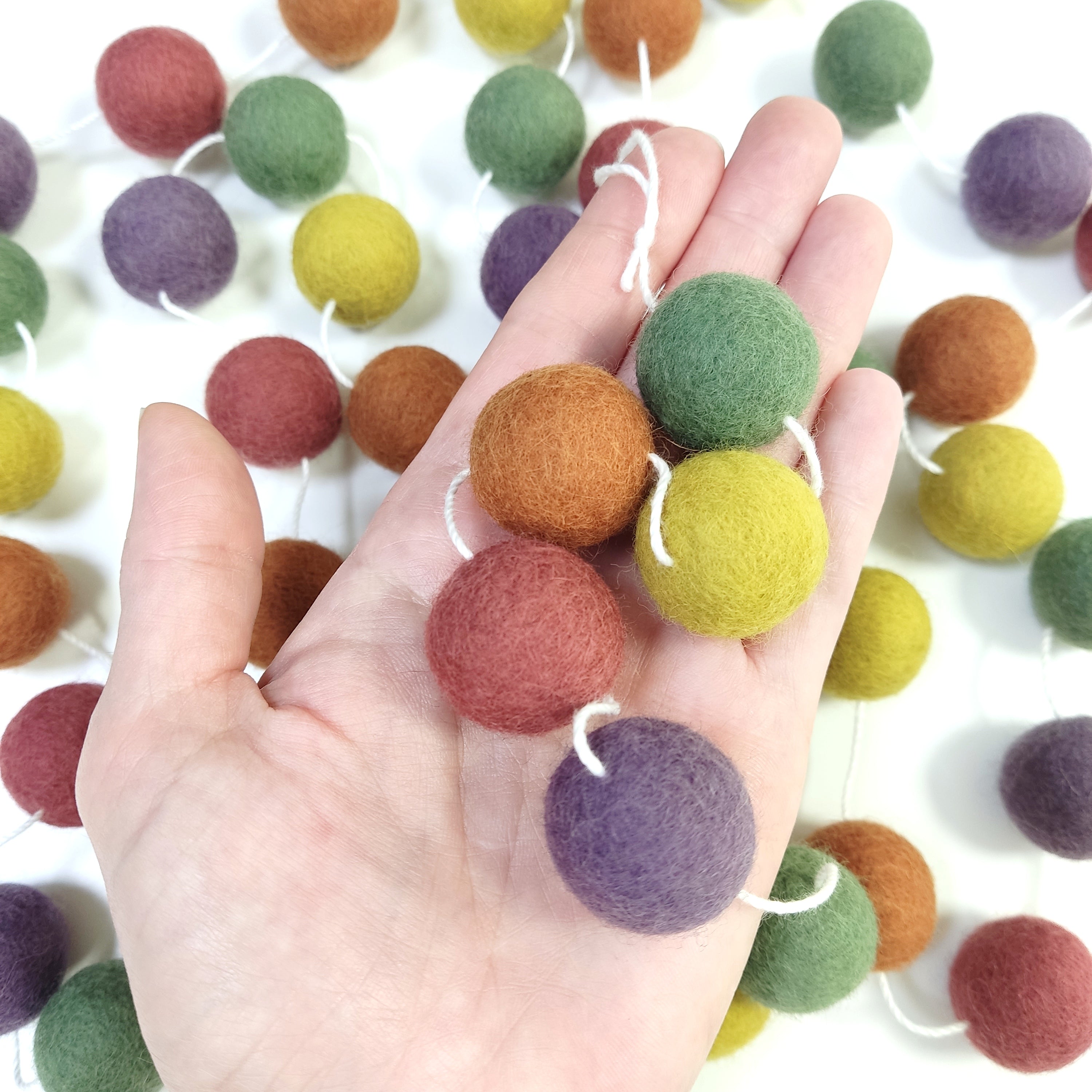 Zoom sur les pompons en feutre de laine mérinos de 2,5 cm de la guirlande multicolore vintage dans une main