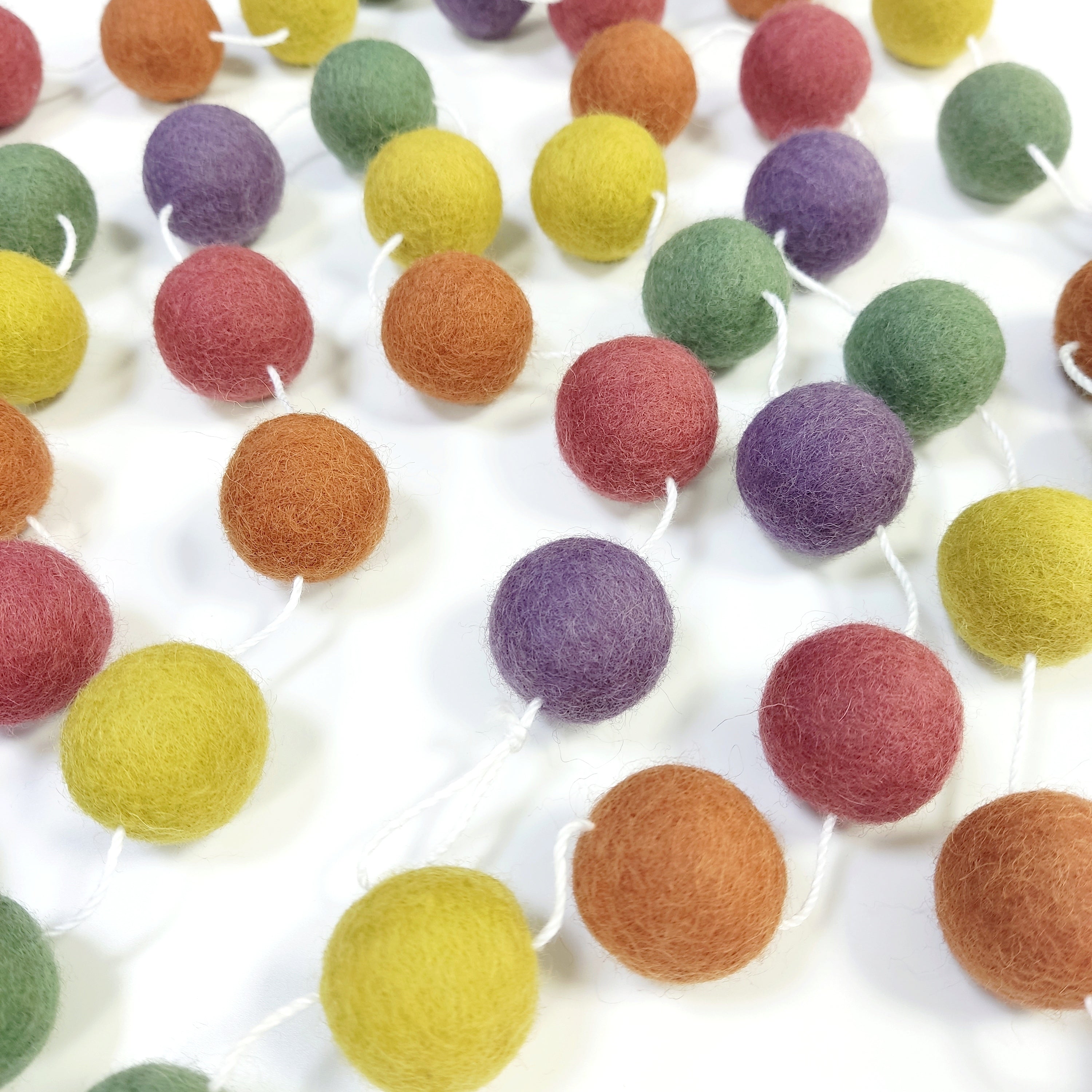 Guirlande en boules de laine feutrée multicolore vintage étalée sur une table avec les pompons espacés