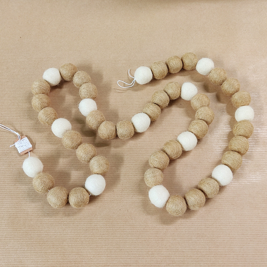 Zoom sur les pompons feutrés beige poudré et blanc naturel de la guirlande de Noël scandinave