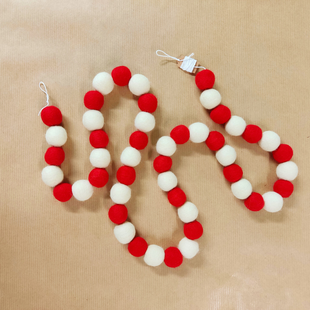 Zoom sur les pompons feutrés rouge coquelicot et blanc neige de la guirlande de Noël artisanale