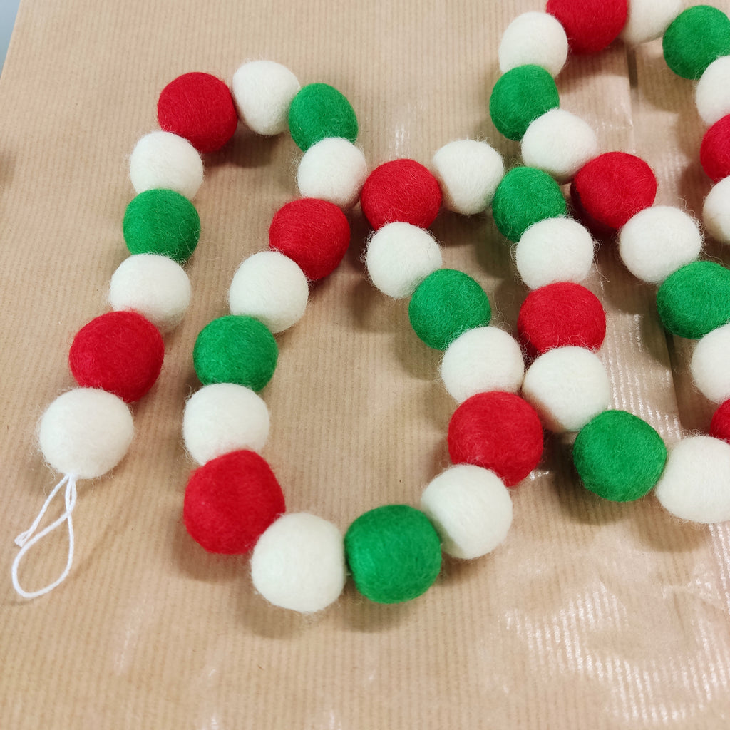 Guirlande de pompons Noël rouge blanc vert étalée sur une table vue de dessus