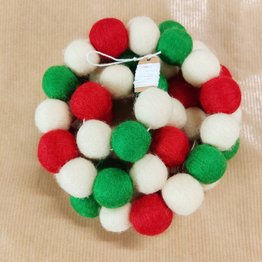 Zoom sur les pompons feutrés rouge coquelicot, blanc neige et vert herbe de la guirlande de Noël