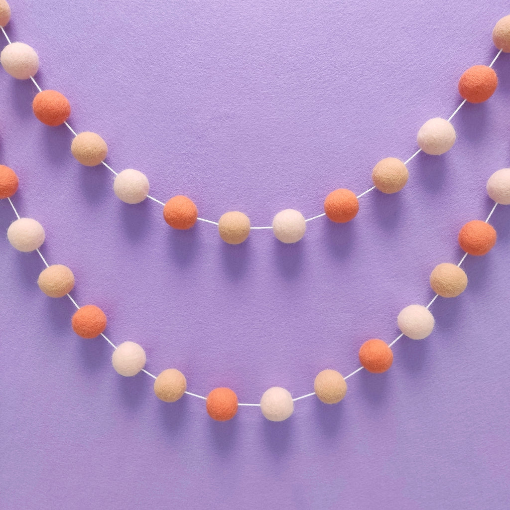 Guirlande de pompons en laine mérinos orange flamingo accrochée au mur