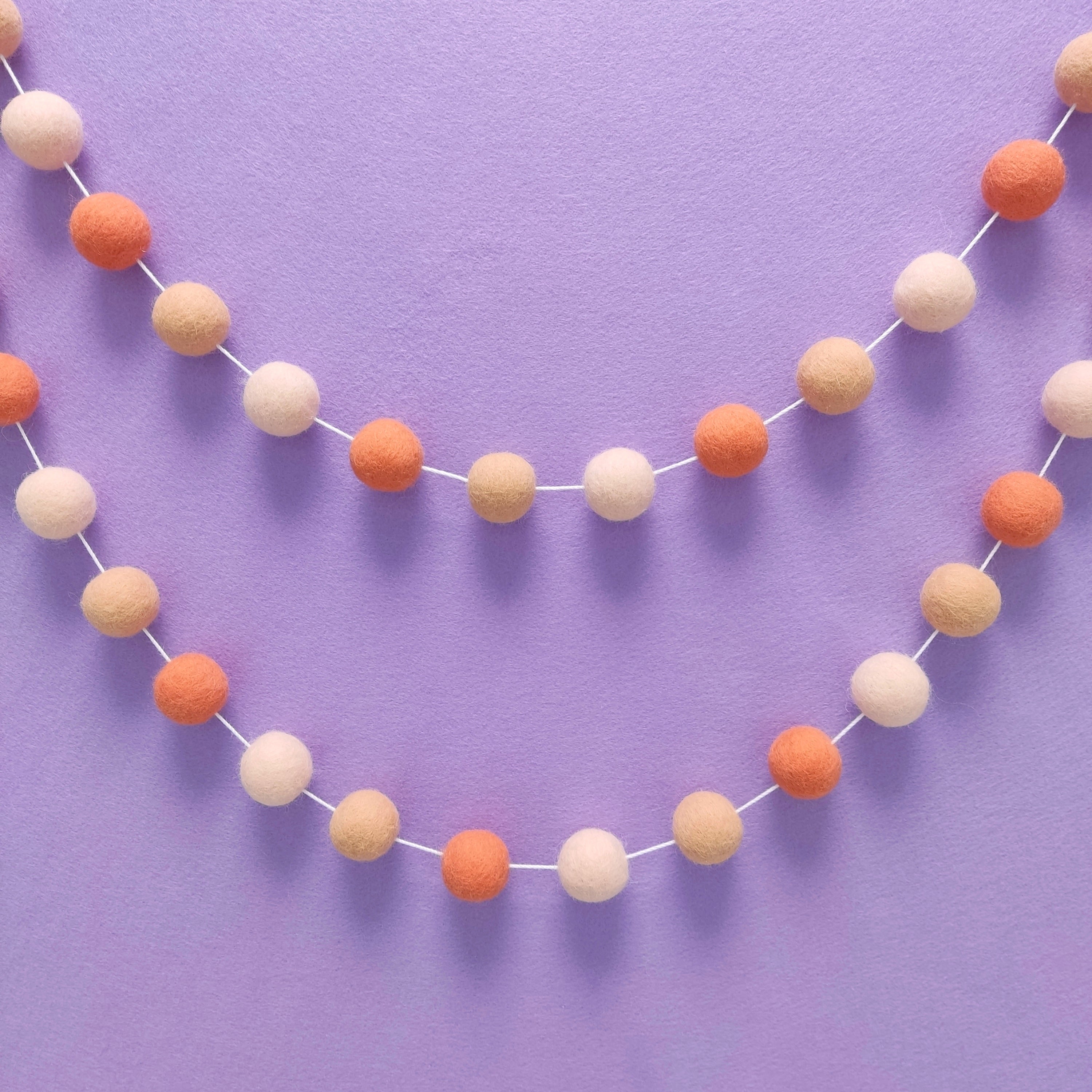 Guirlande de pompons en laine mérinos orange flamingo accrochée au mur