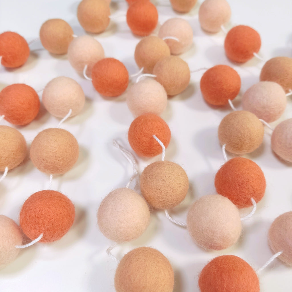 Guirlande en boules de feutre orange flamingo étalée sur une table avec les pompons espacés