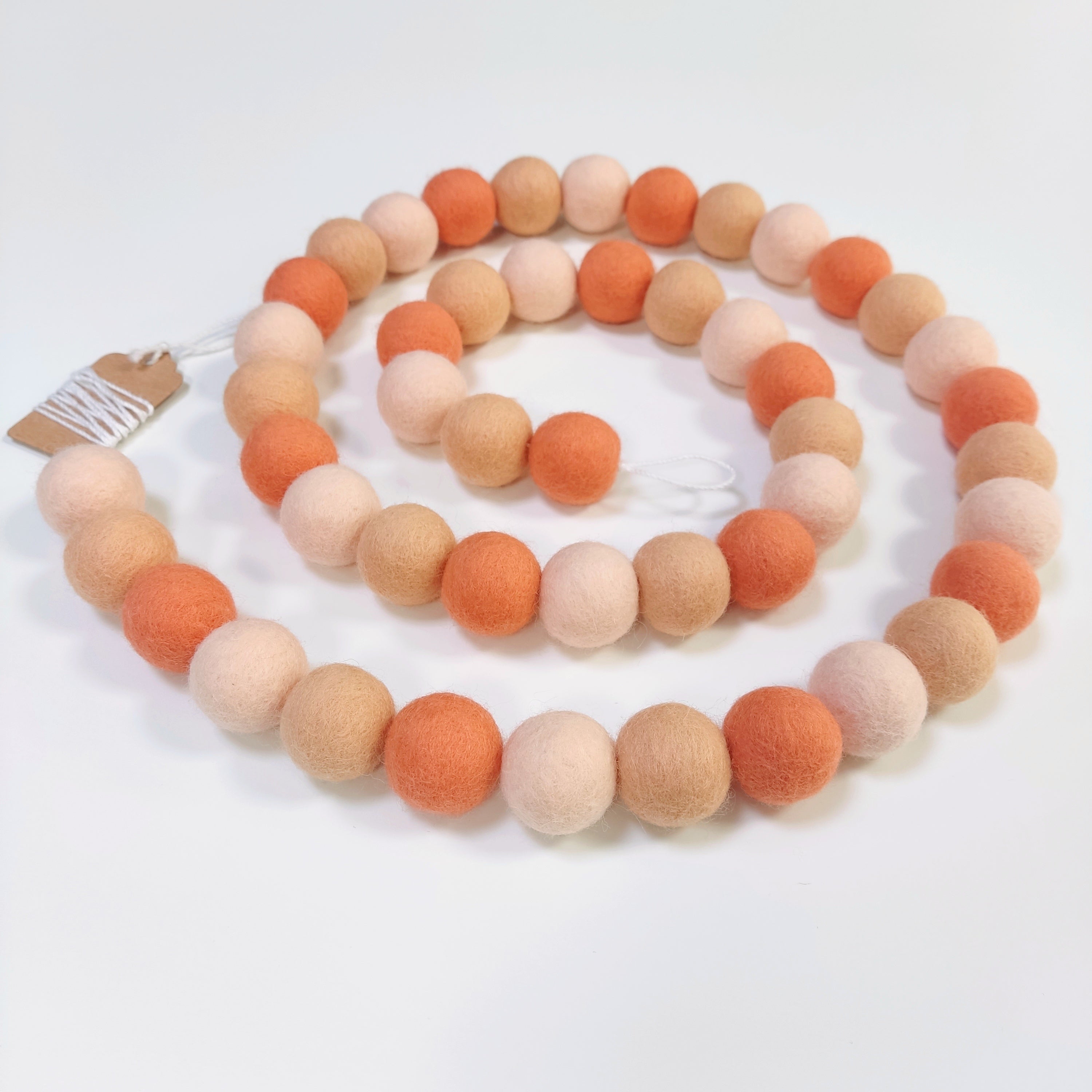 Guirlande de pompons feutrés orange flamingo disposée en spirale sur une table vue de dessus