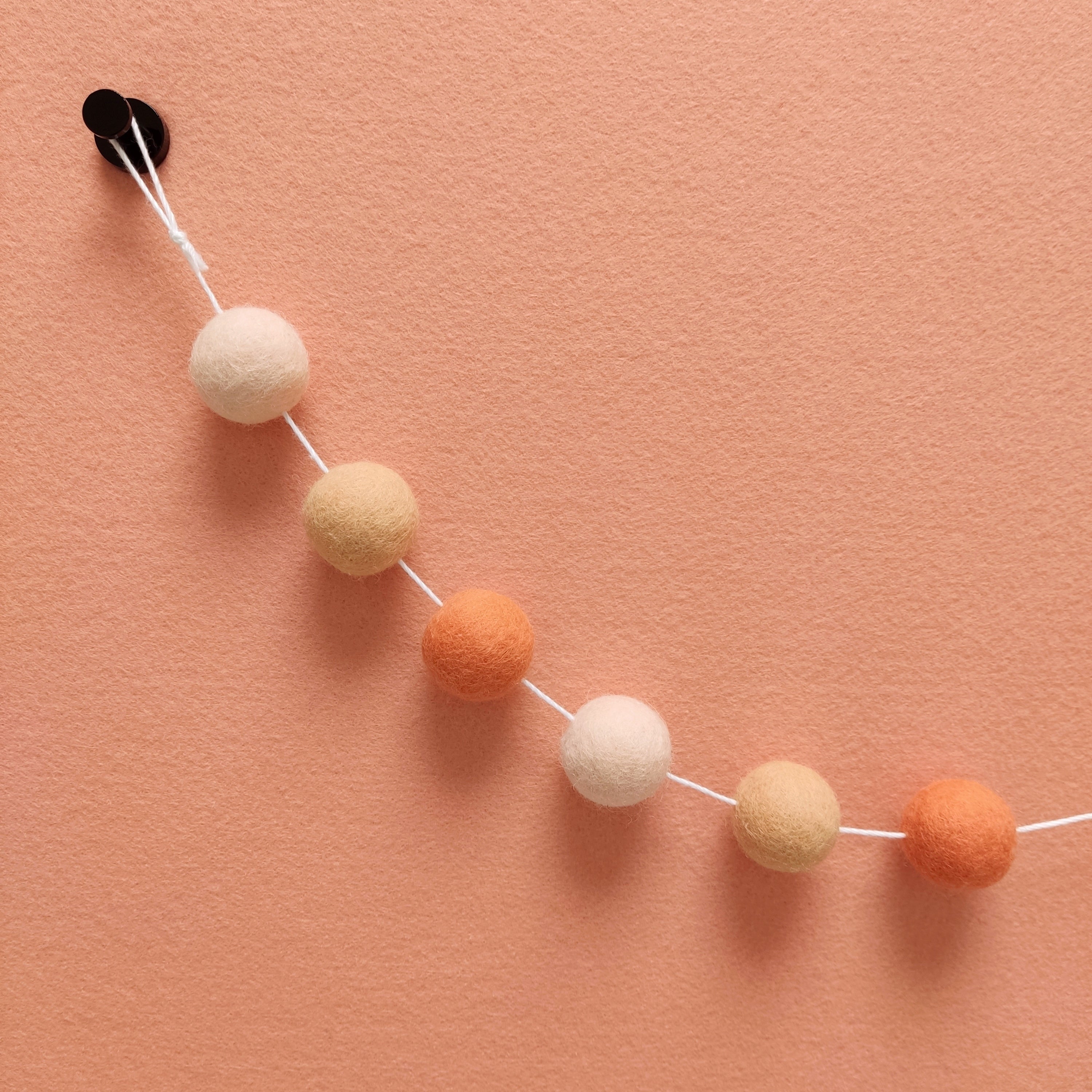 Zoom sur les 3 couleurs de la guirlande de pompons orange flamingo ainsi que sa boucle de fixation