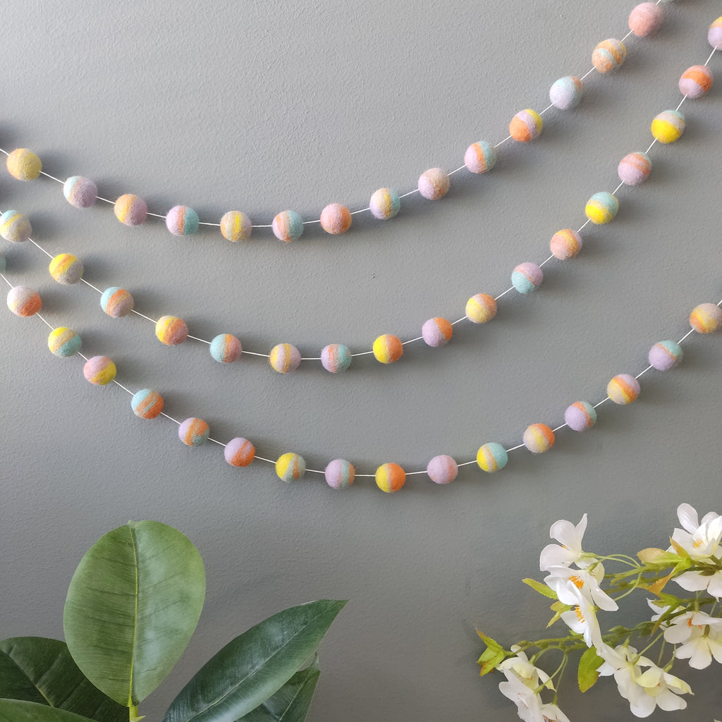 Guirlande de pompons pastel mix fixée au mur vue de loin pour décoration chambre enfant
