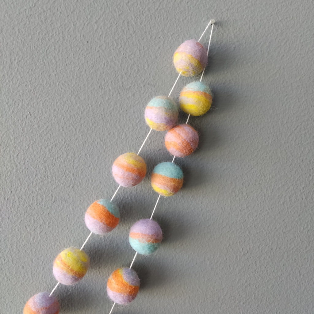 Zoom sur les couleurs de la guirlande en boules de feutre pastel mix : jaune citron, bleu aqua, orange carotte et lavande