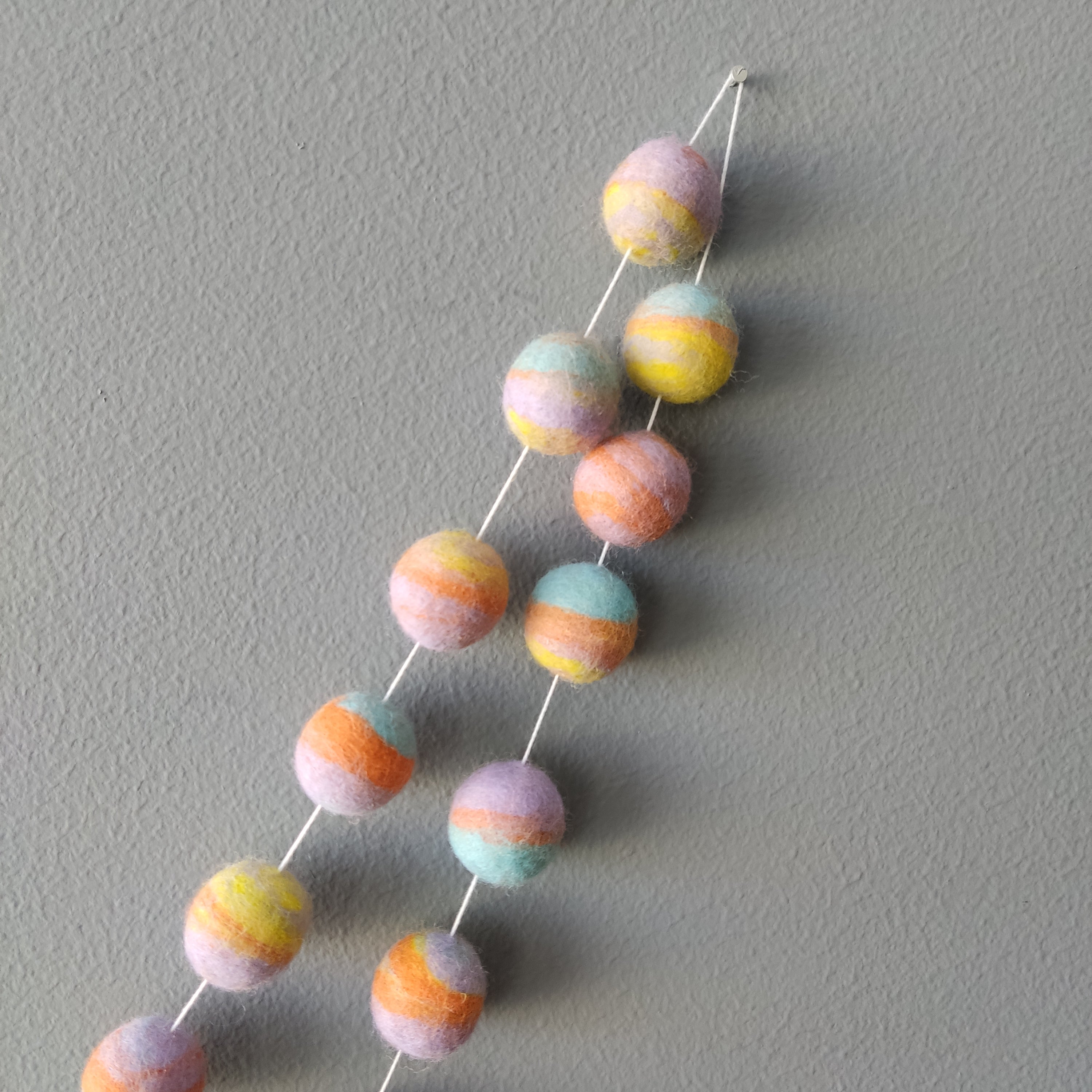 Zoom sur les couleurs de la guirlande en boules de feutre pastel mix : jaune citron, bleu aqua, orange carotte et lavande