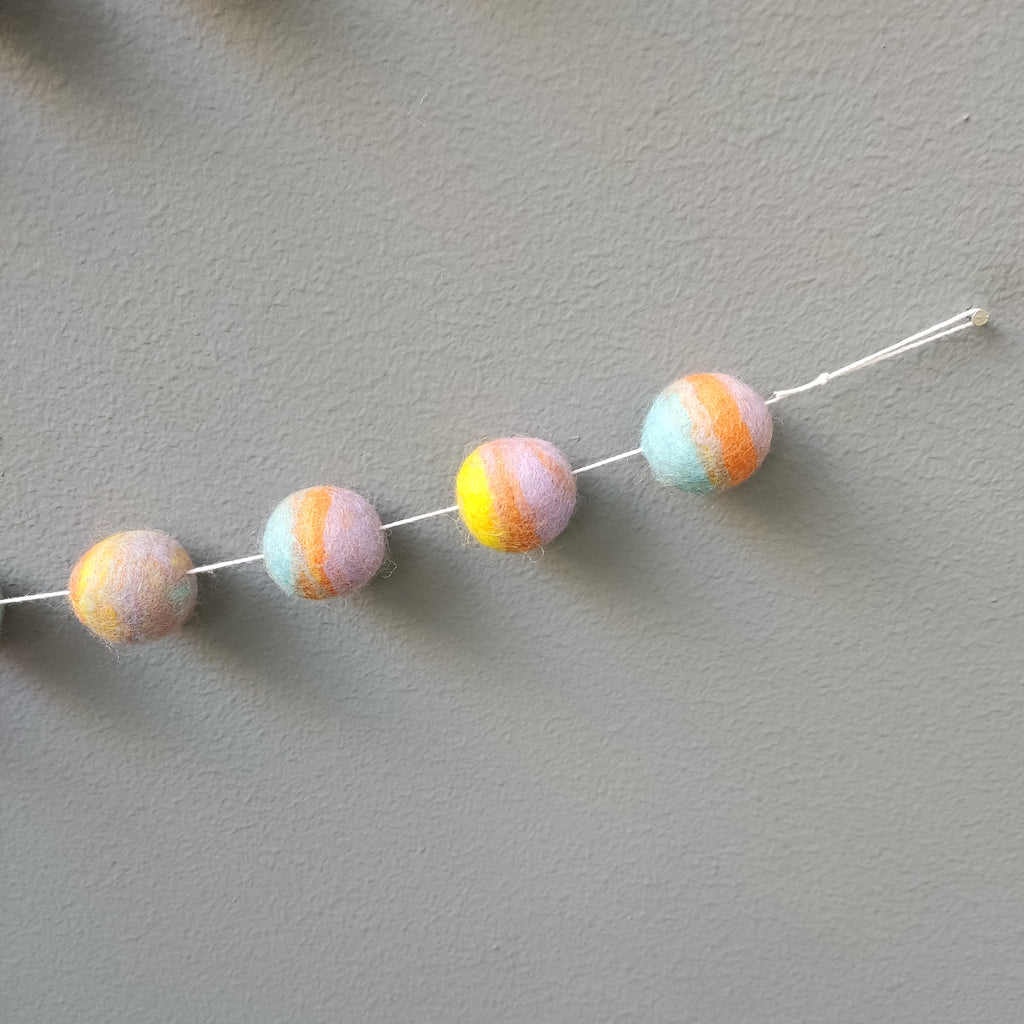 Détail des pompons feutrés en laine mérinos de la guirlande pastel mix avec boucle de fixation