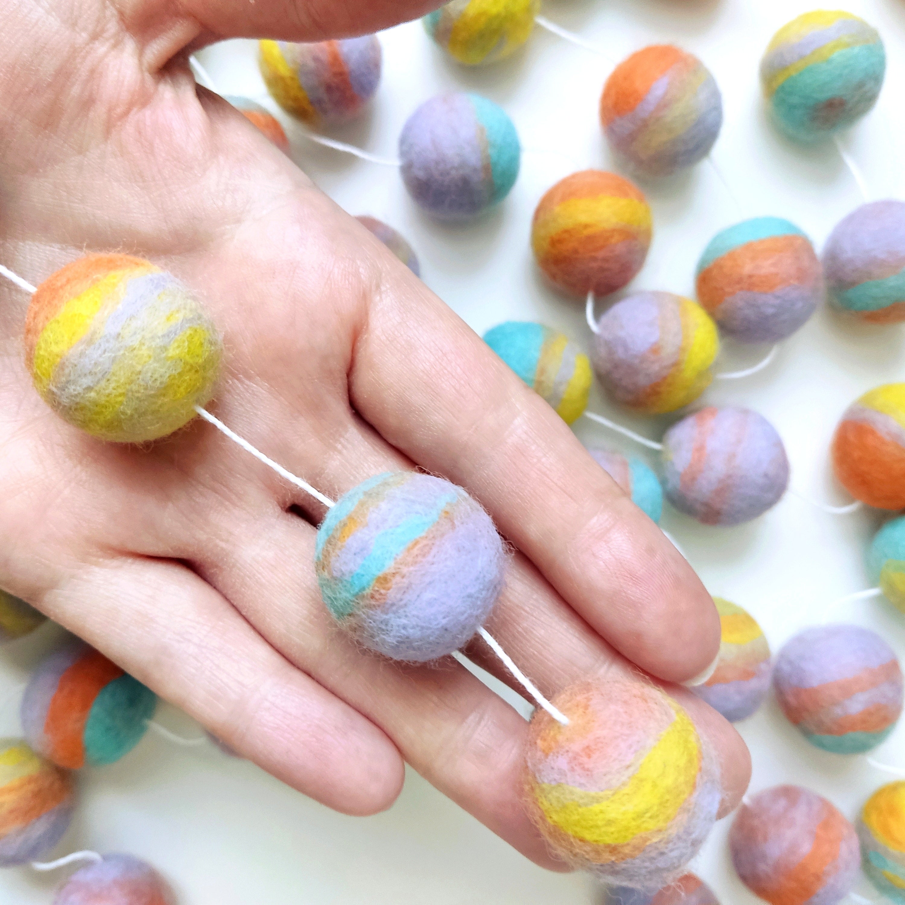 Détail des pompons feutrés de la guirlande pastel mix dans une main