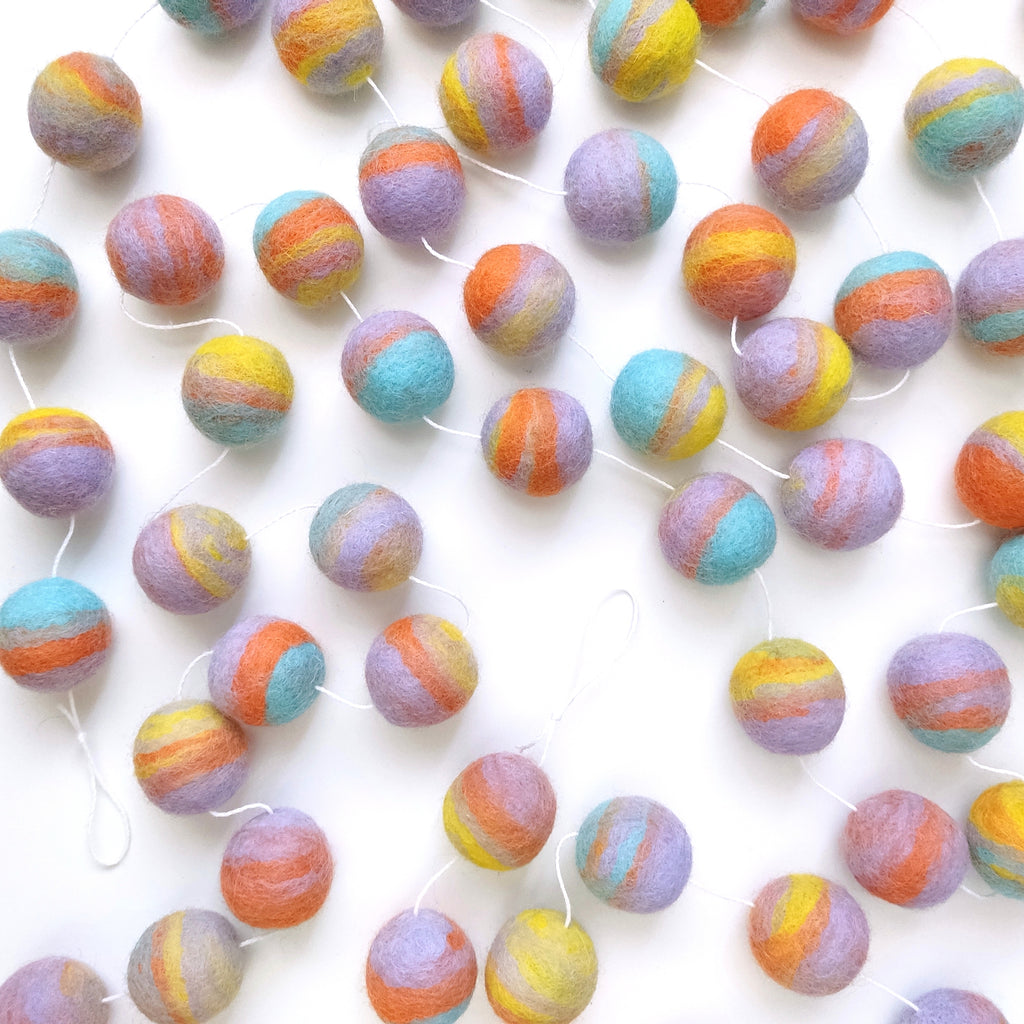 Guirlande de pompons en feutre pastel mix étalée sur une table avec les pompons espacés