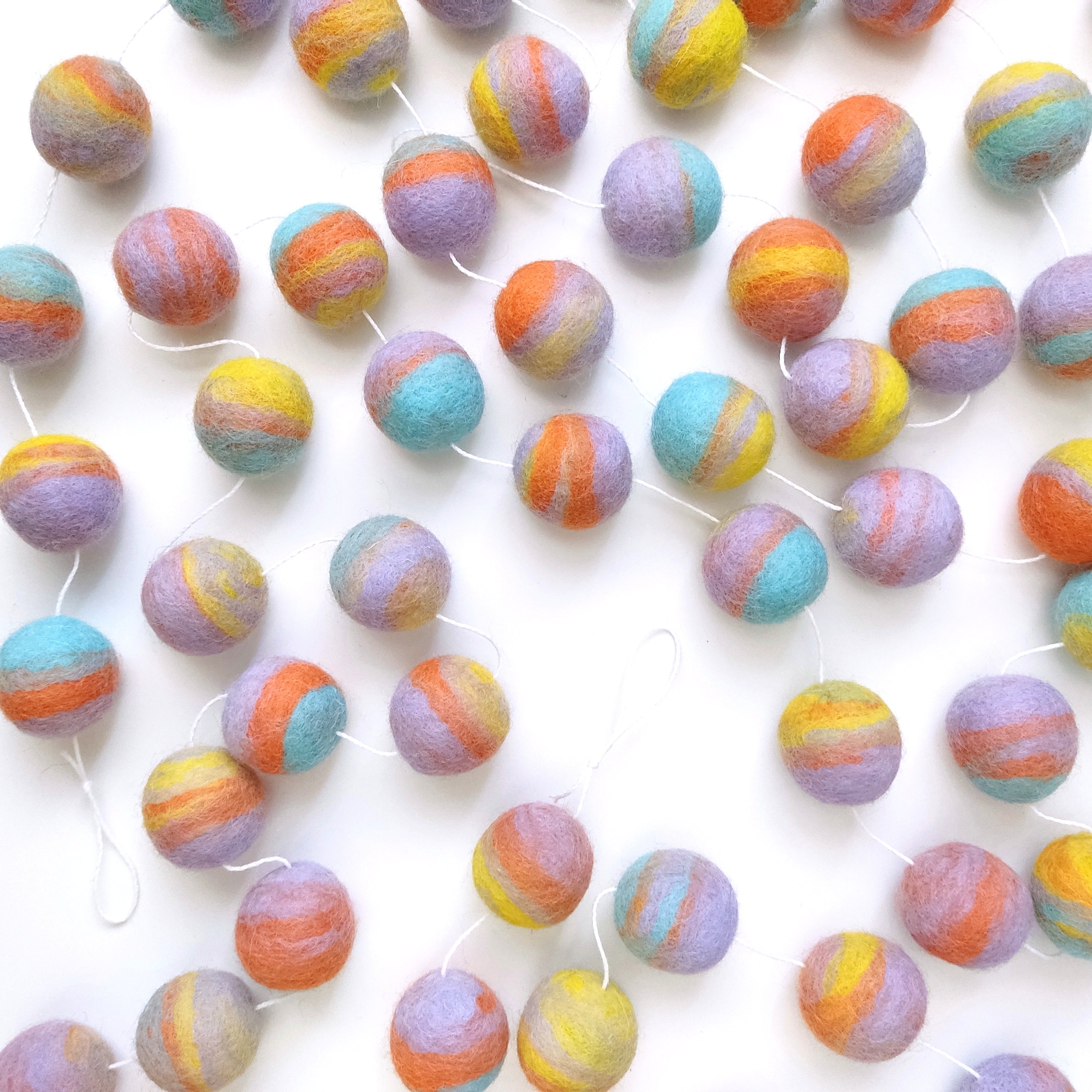 Guirlande de pompons en feutre pastel mix étalée sur une table avec les pompons espacés