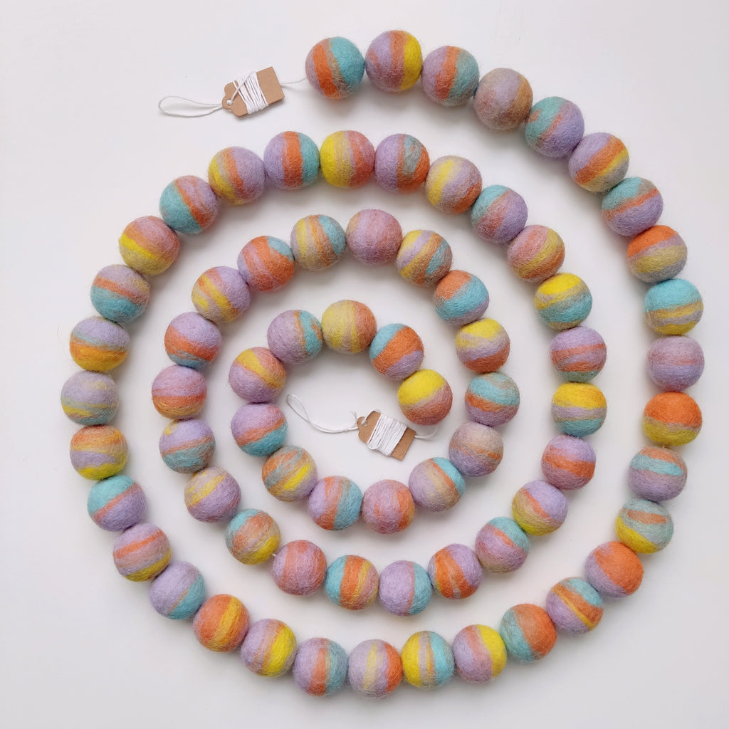 Guirlande de pompons de feutre pastel mix disposée en spirale sur une table vue de dessus