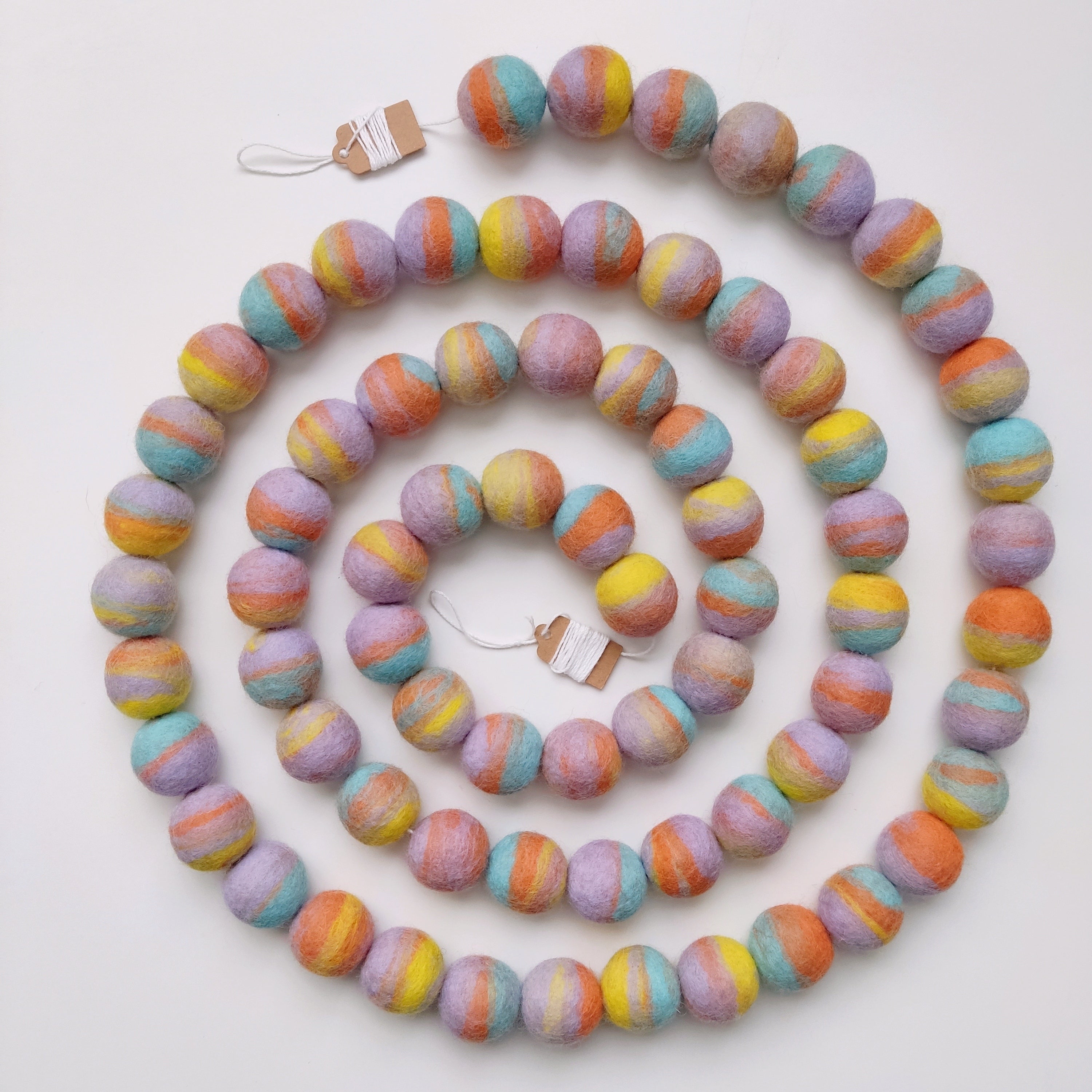 Guirlande de pompons de feutre pastel mix disposée en spirale sur une table vue de dessus