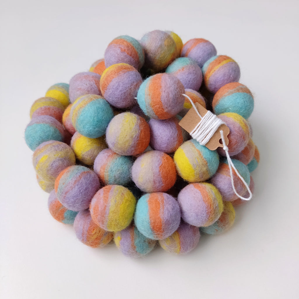 Zoom sur la guirlande en boules de laine feutrée pastel mix avec étiquette