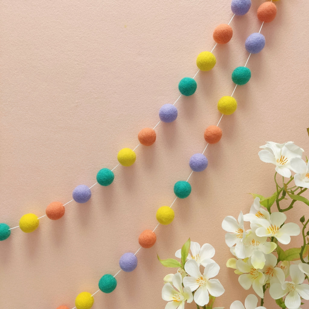 Guirlande en boules de feutres pastel pop fixée sur un mur