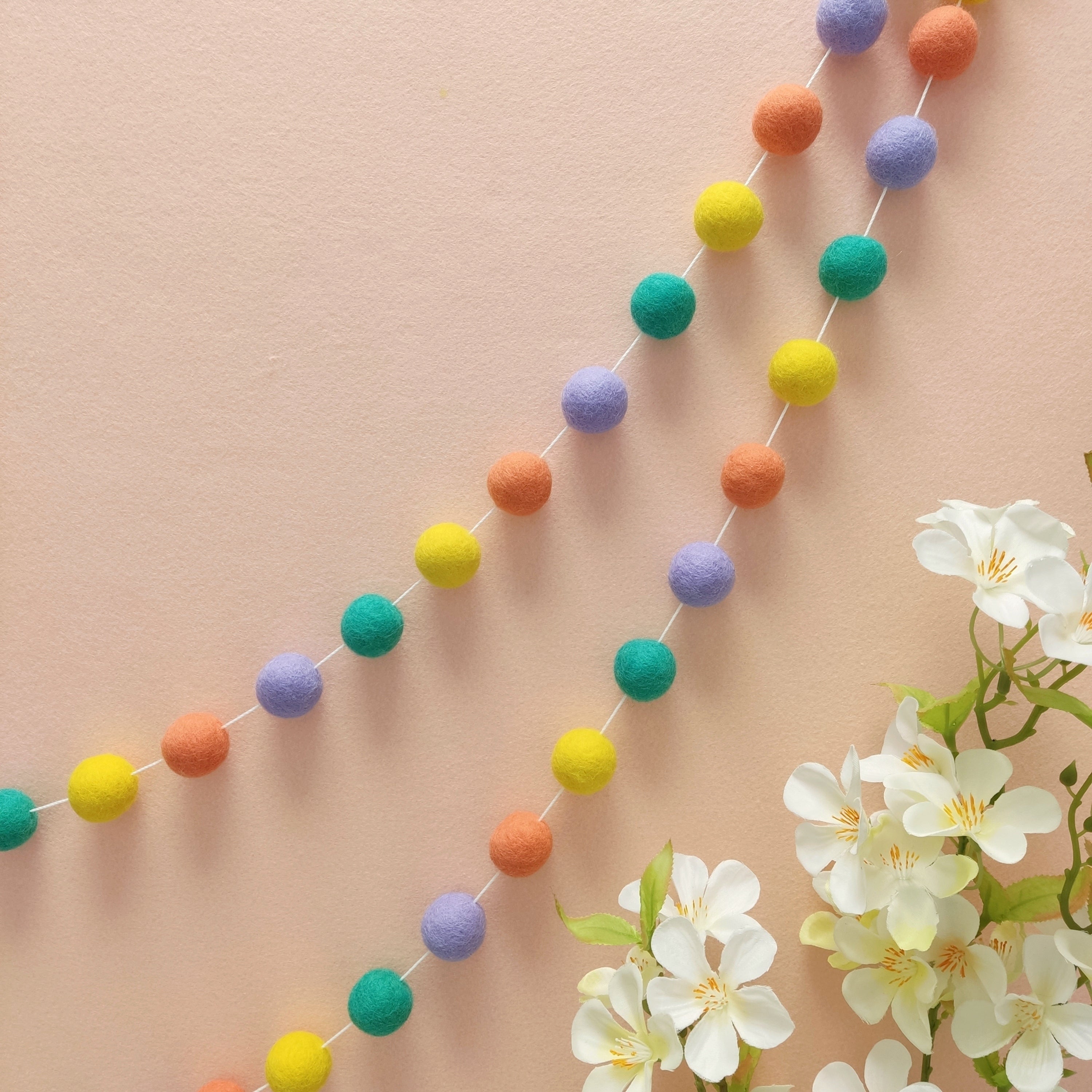 Guirlande en boules de feutres pastel pop fixée sur un mur