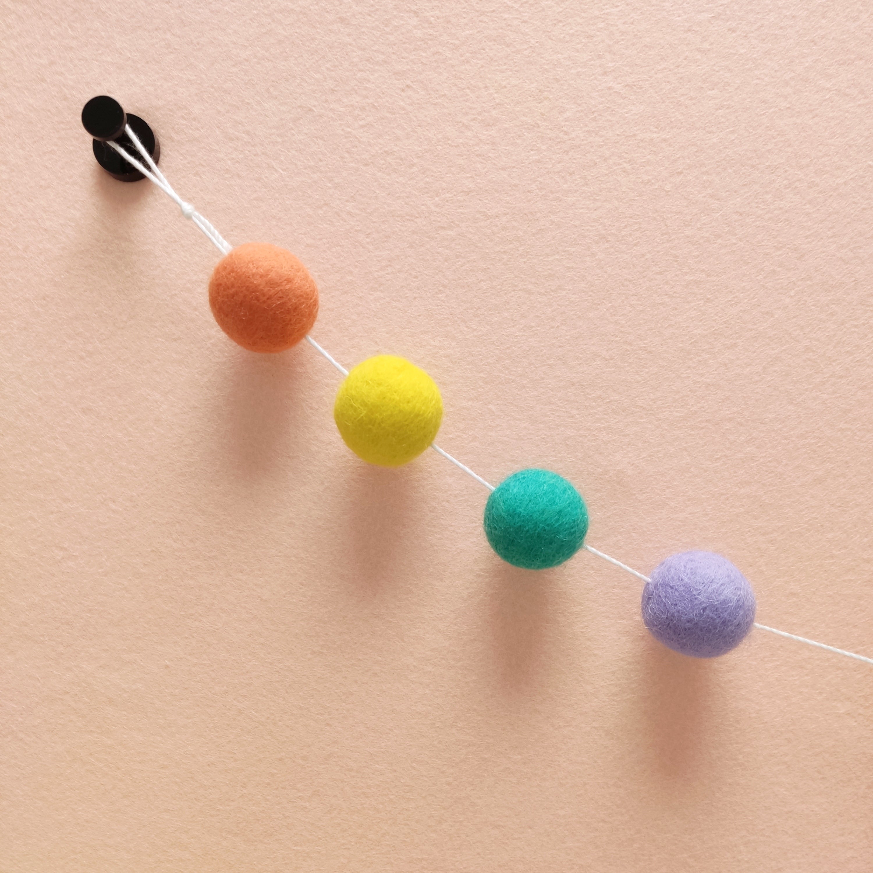 Zoom sur les pompons jaune citron, vert lagon, orange flamingo et lavande de la guirlande pastel pop