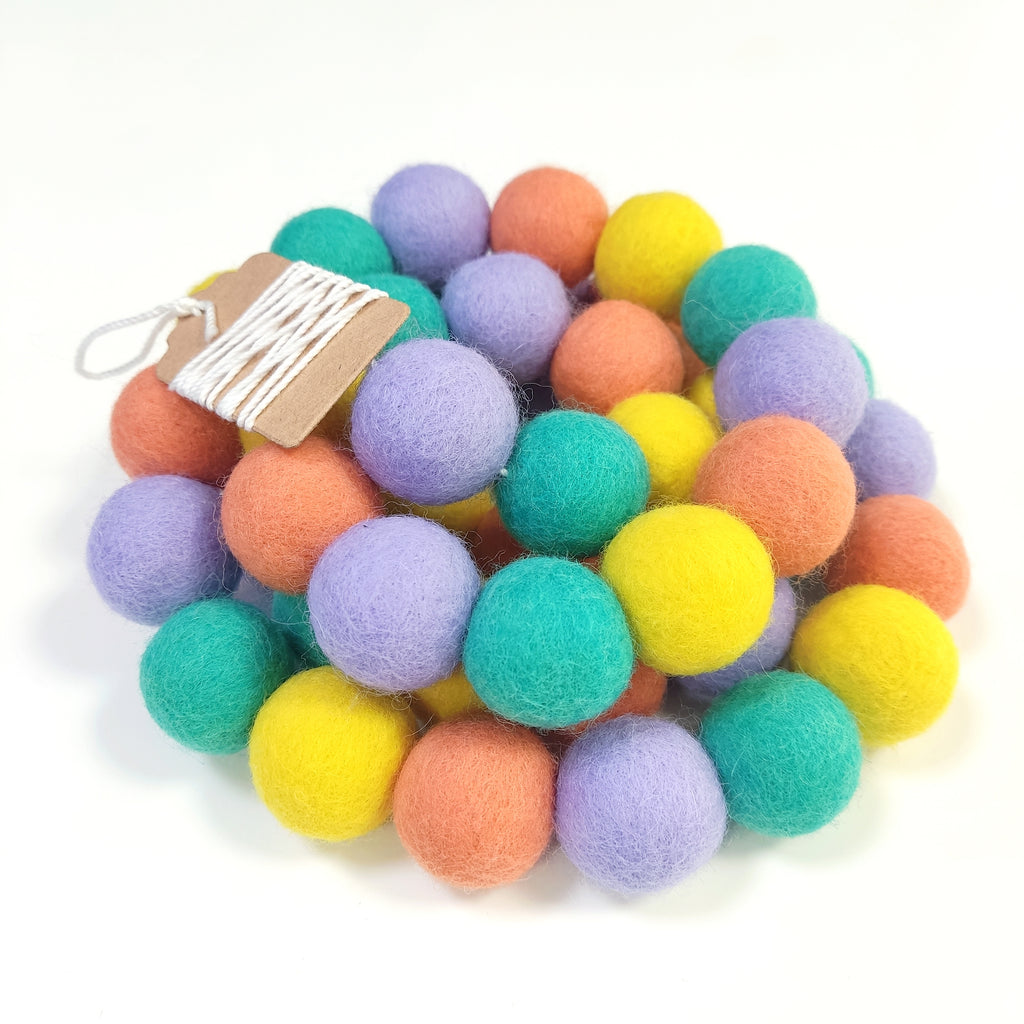 Zoom sur la guirlande de pompons en feutre jaune orange lavande et vert lagon avec étiquette