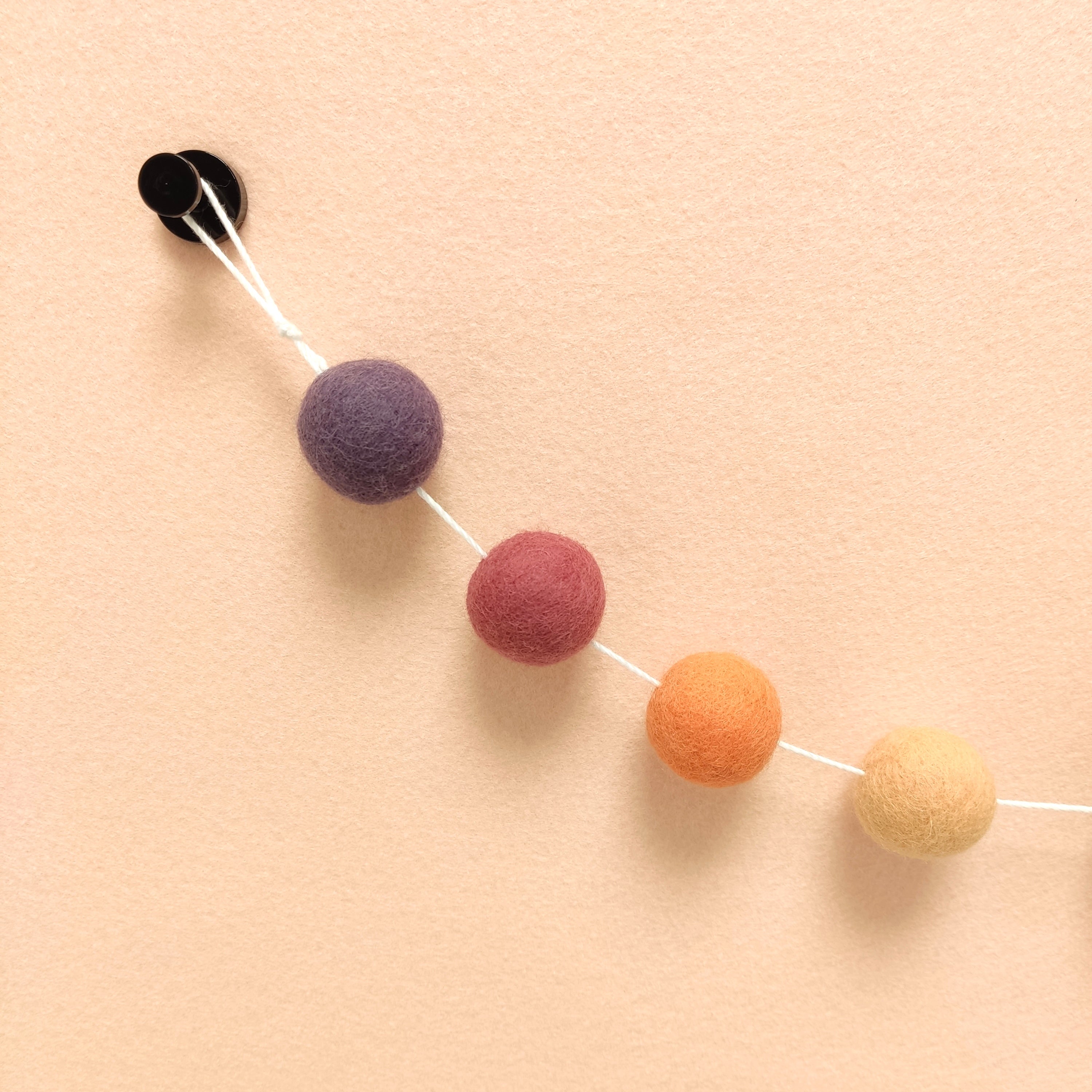 Zoom sur les 4 couleurs de la guirlande de pompons feutrés orange pêche, orange flamingo, rose boisé et améthyste.