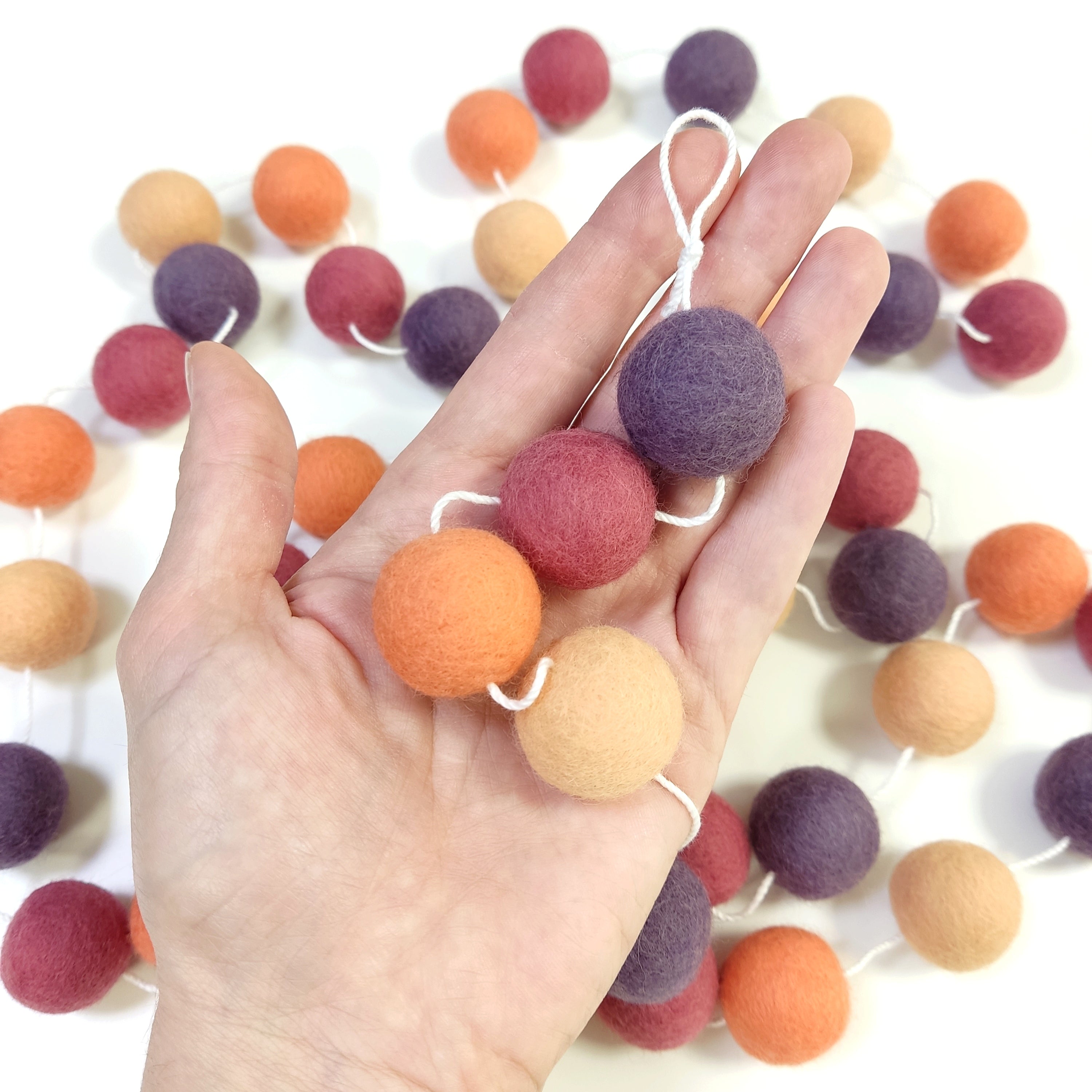 Détail des pompons en feutre de laine mérinos orange pêche, orange flamingo, rose boisé et violet améthyste dans une main
