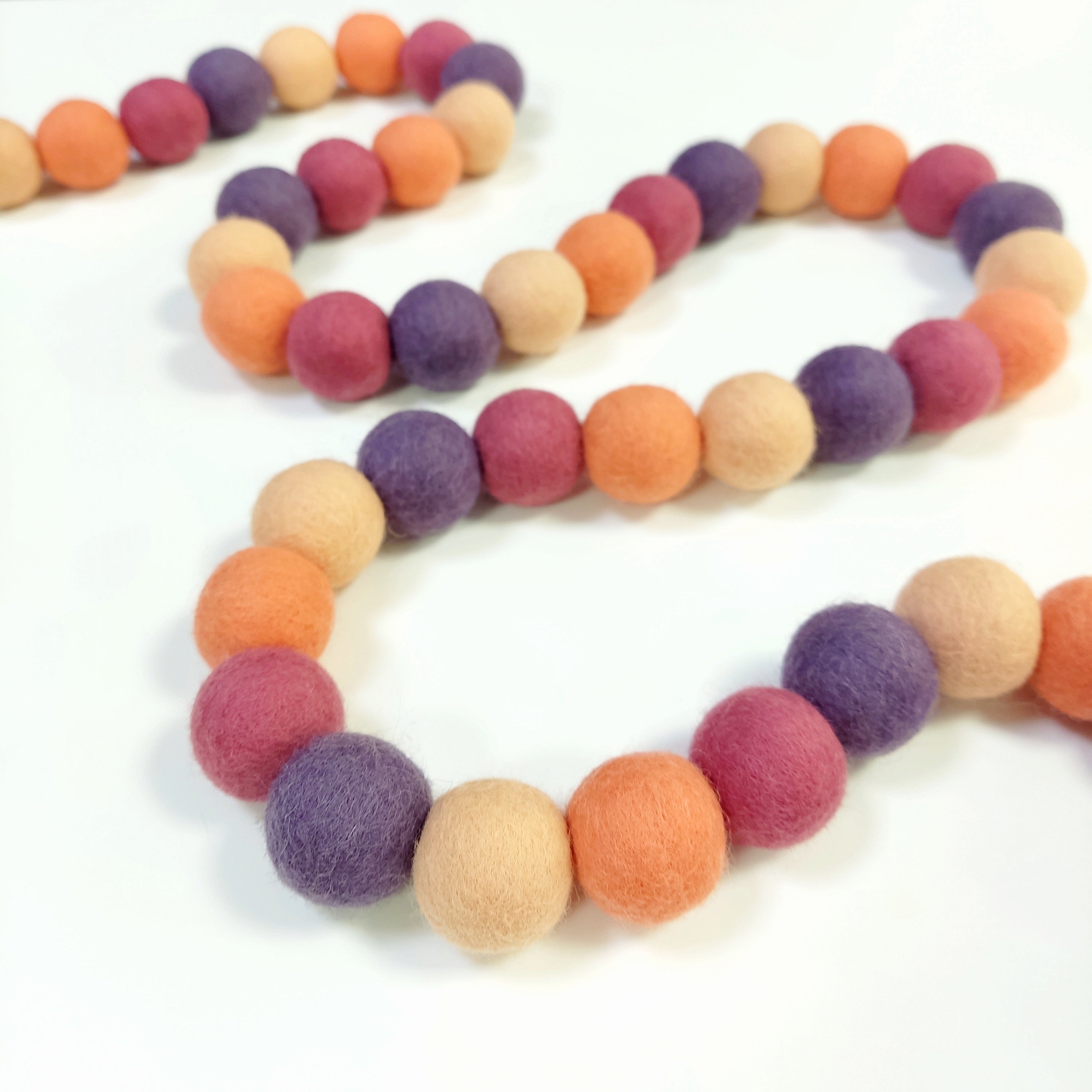 Guirlande en boules de feutre pêche améthyste disposée en serpentin sur une table avec les pompons rassemblés sur le fil