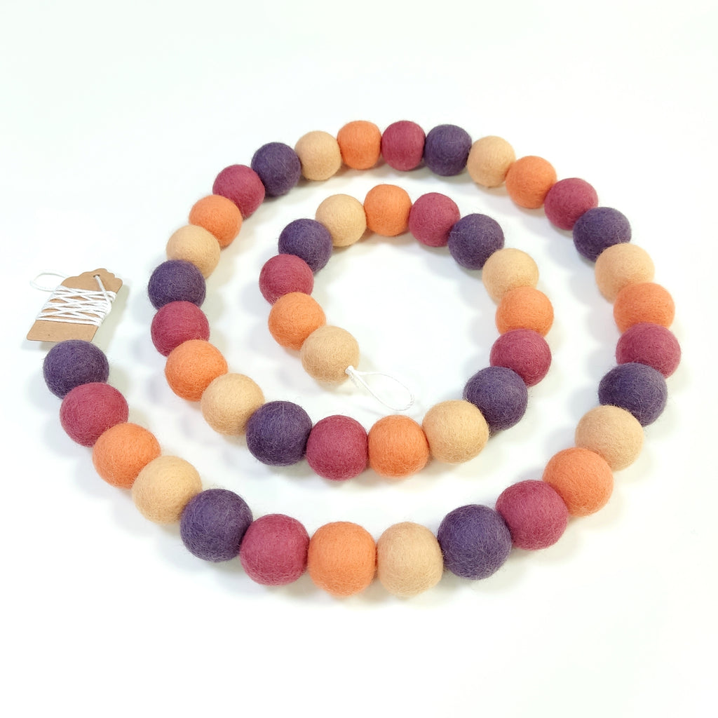 Guirlande de pompons de laine feutrée rose orange améthyste posée en spirale sur fond blanc vue de près